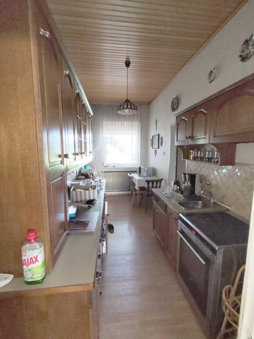 Schmale Küche mit Holzschränken, Fenster und einfacher Ausstattung.