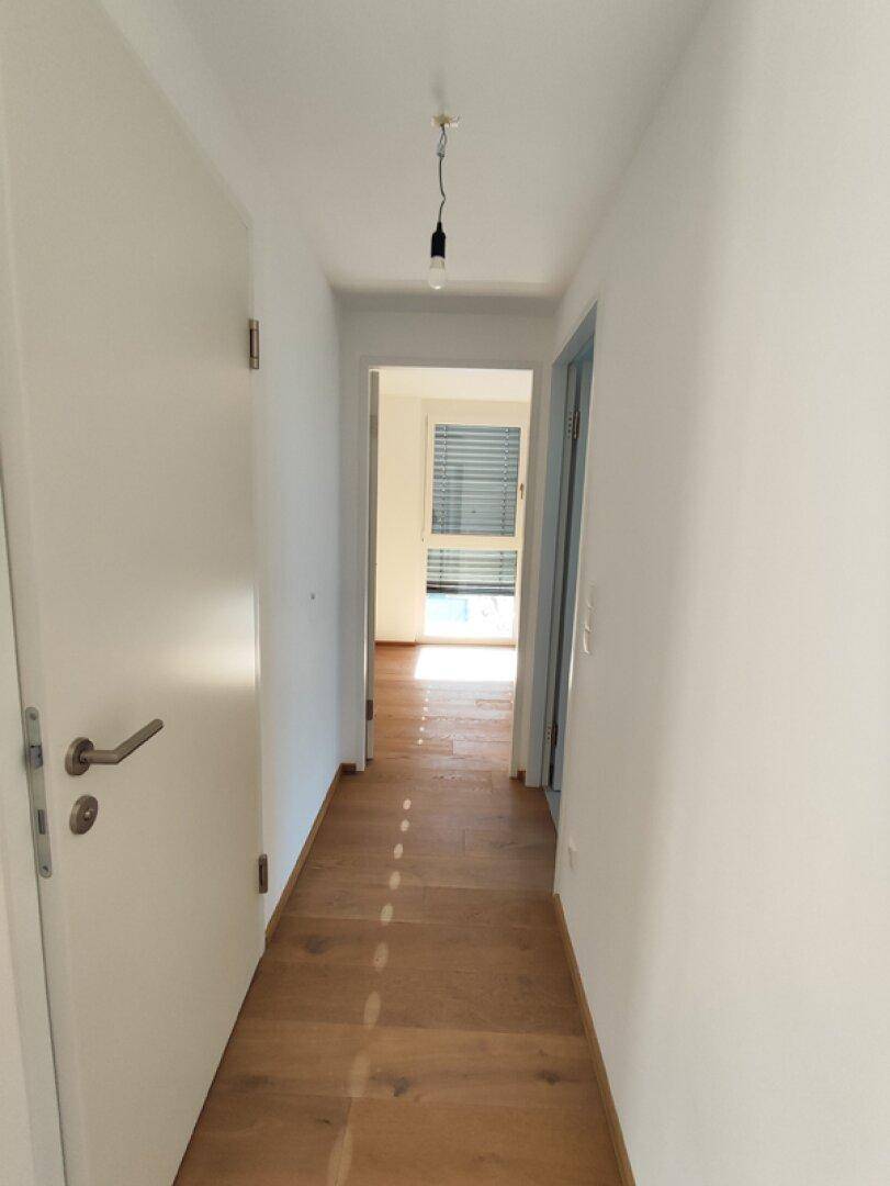 Heller Flur mit Holzboden und weißen Wänden, der zu weiteren Räumen führt.