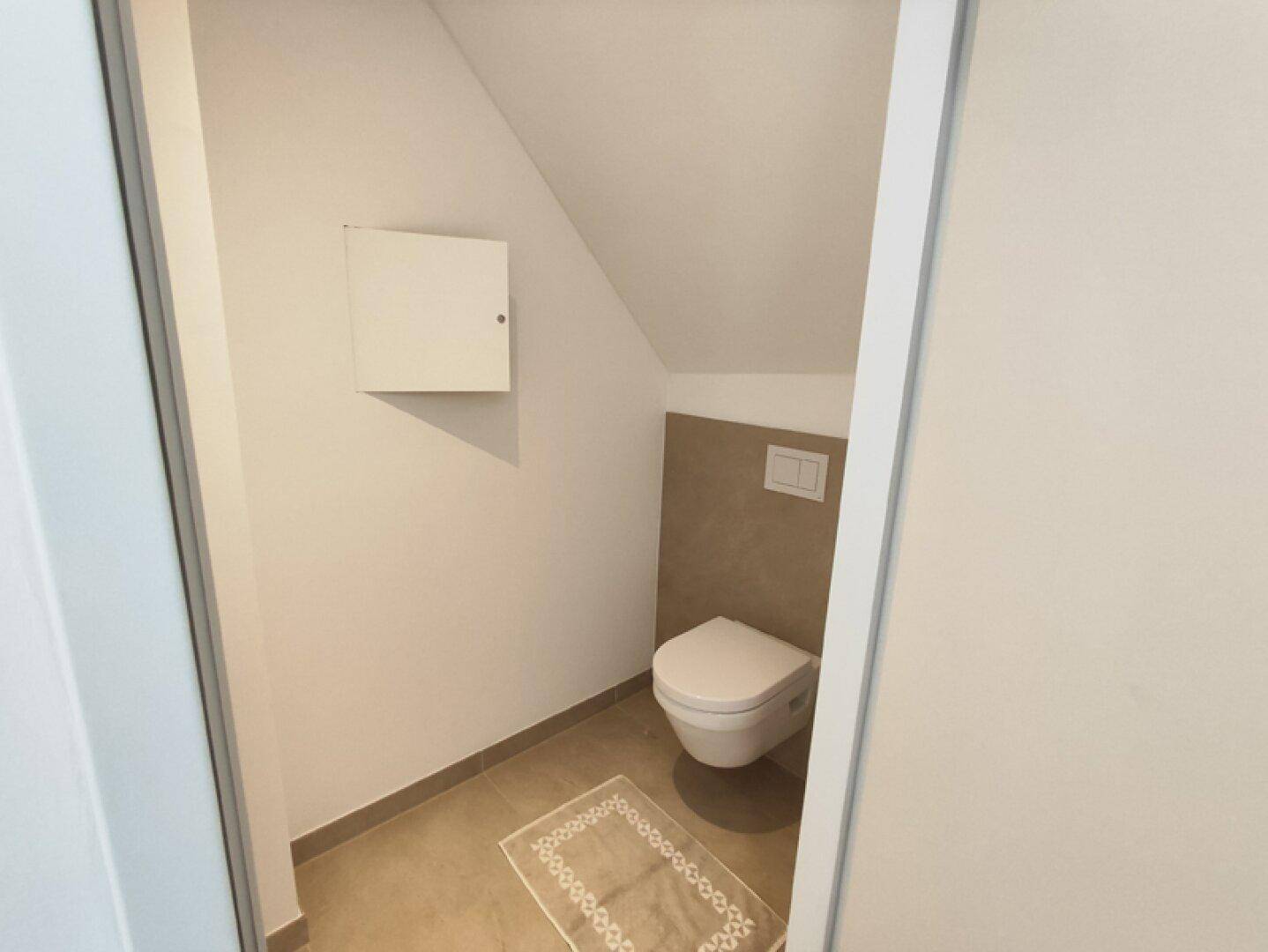 Kleines Gäste-WC mit Wand-WC, Fliesenboden und Dachschräge.