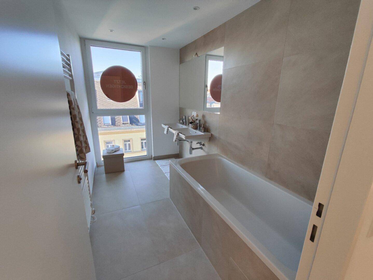 Modernes Badezimmer mit Badewanne, Doppelwaschbecken, Fliesen und großem Fenster.