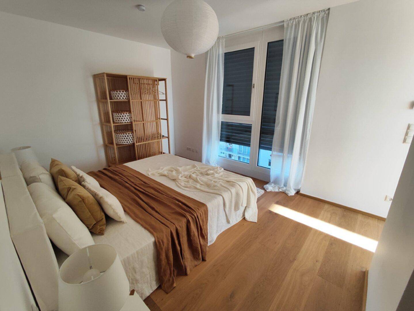 Schlafzimmer mit Holzboden, großem Fenster und hellem, modernem Interieur.