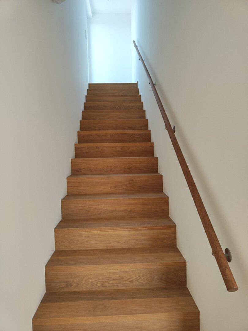 Holztreppe mit Handlauf, die in die obere Etage führt.