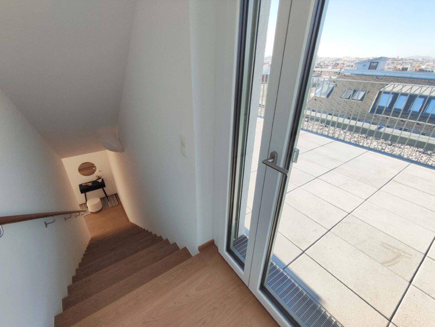 Treppe führt von der Dachterrasse ins Innere, mit Holzdielen und hellem Ambiente.