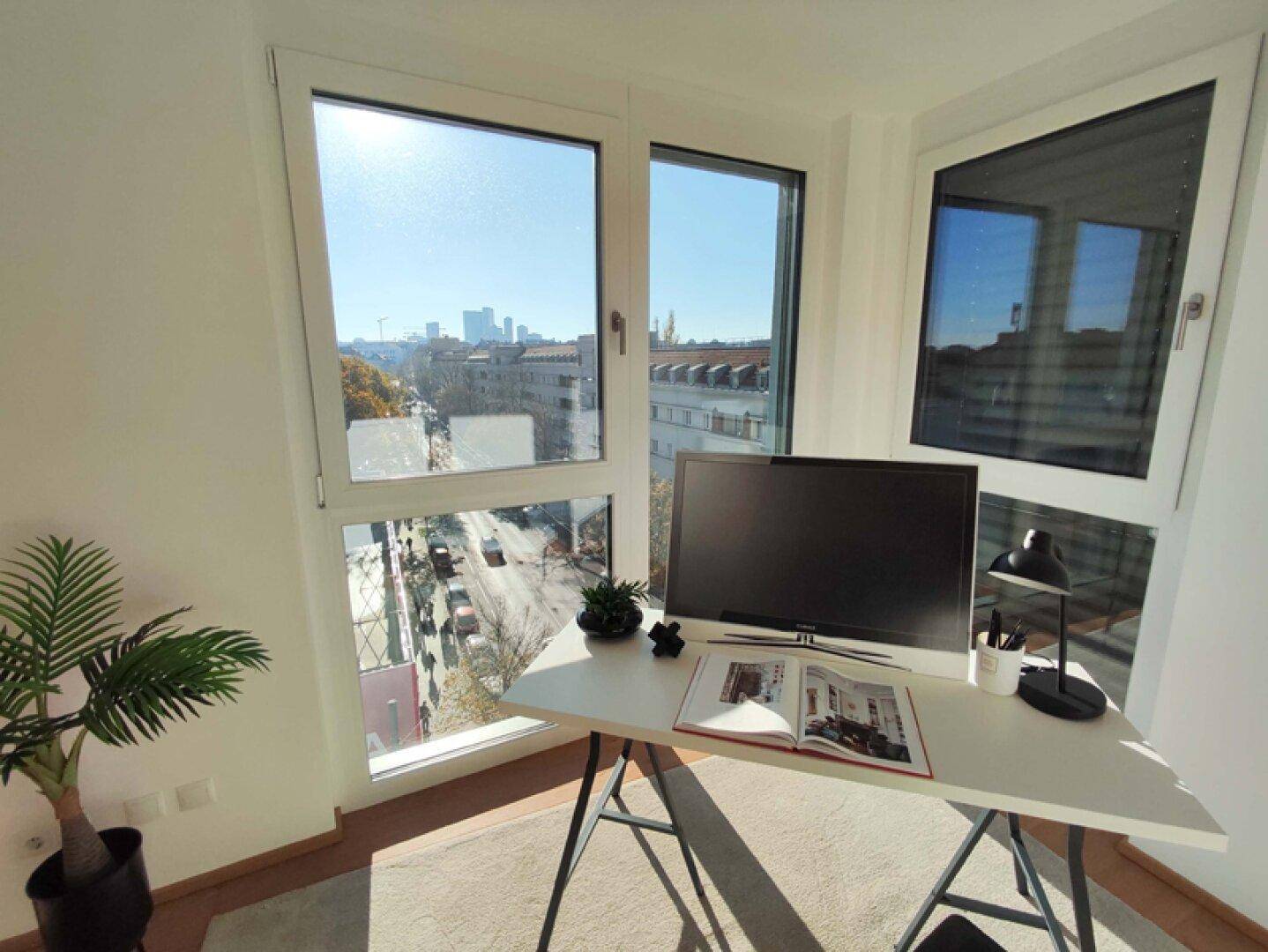 Arbeitszimmer mit Schreibtisch, Holzboden und weitem Stadtblick durch große Fenster.