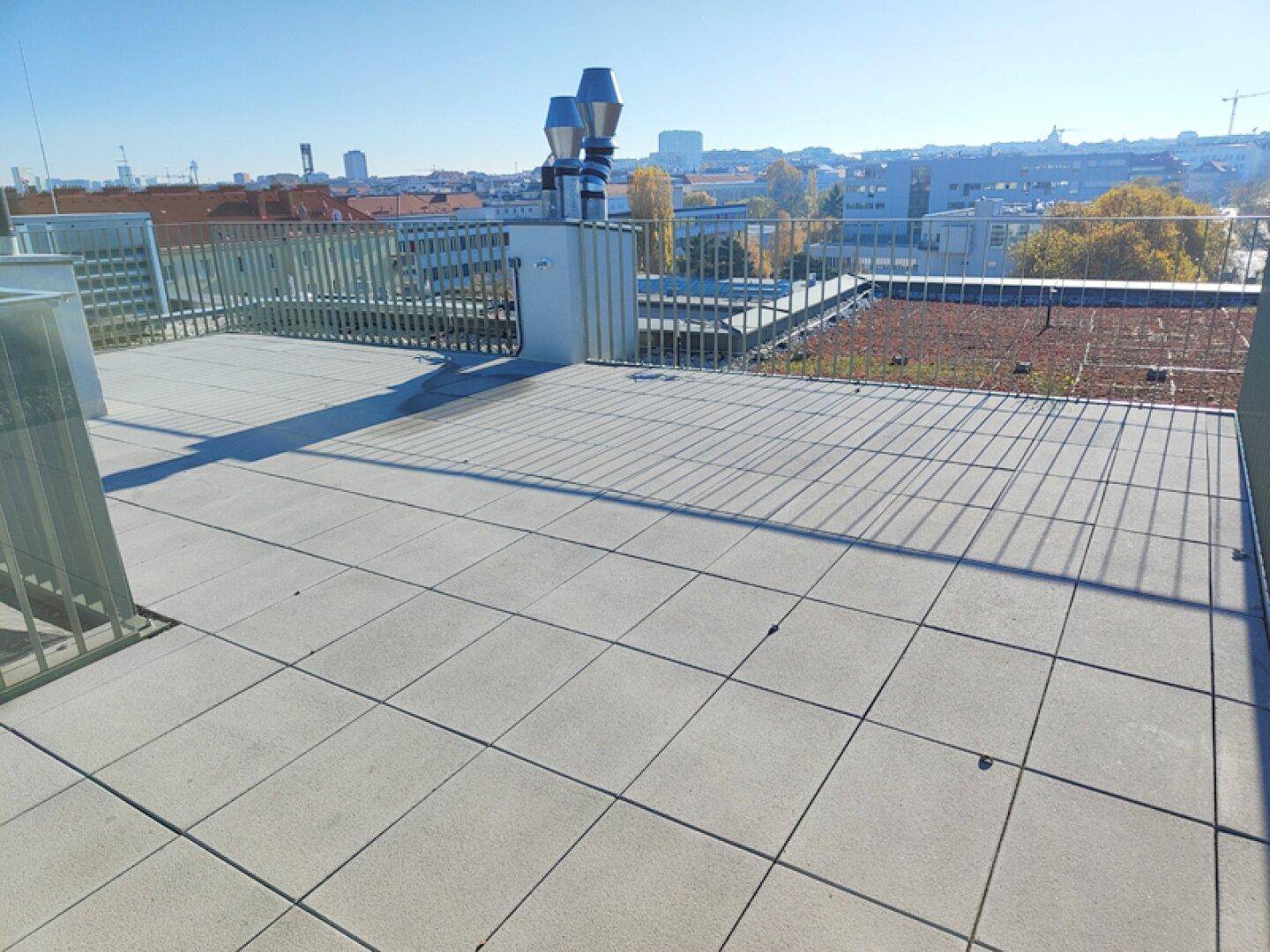 Weitläufige Dachterrasse mit Fliesenboden und Panoramablick über die Stadt.