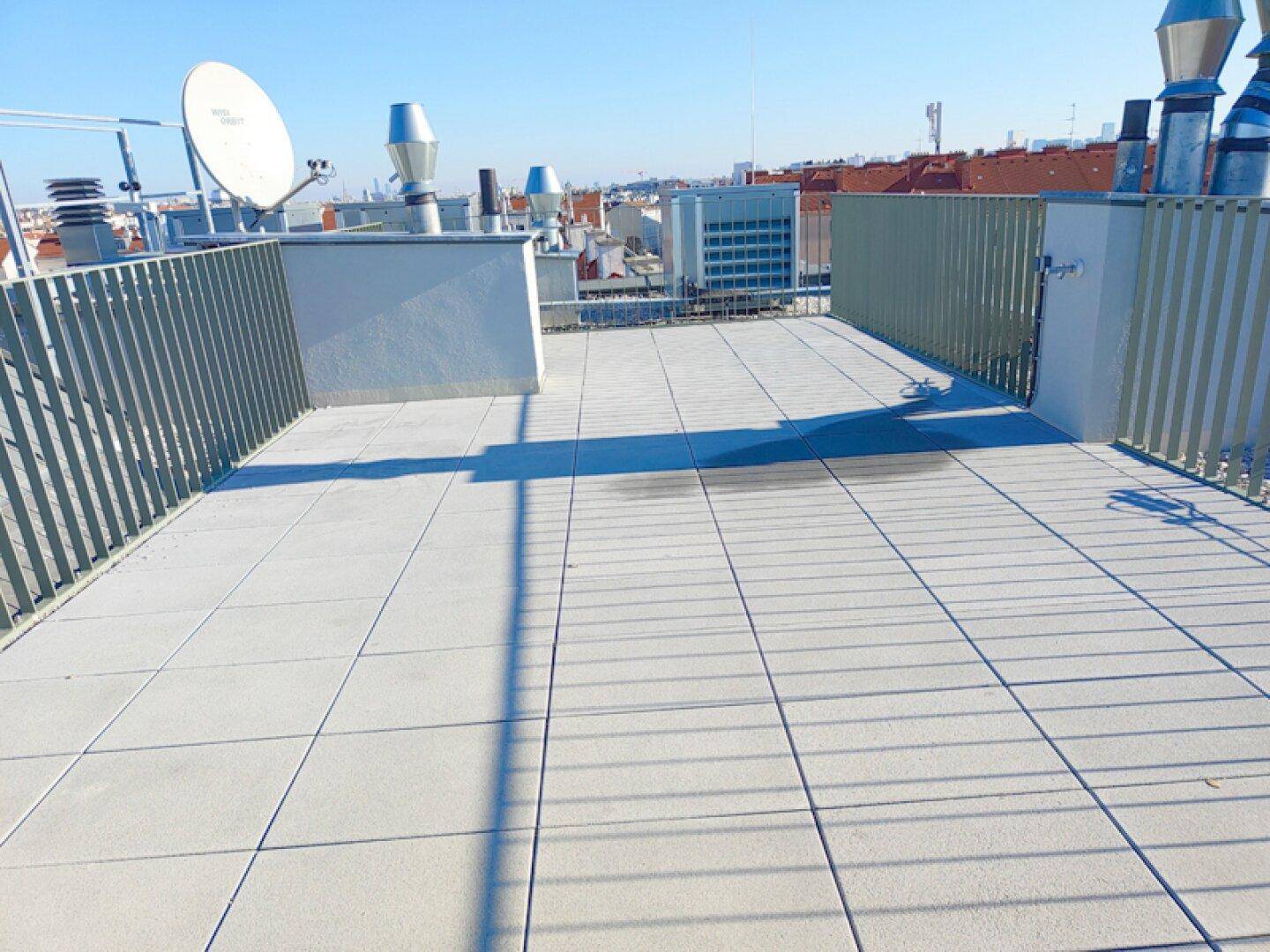 Dachterrasse mit Fliesenboden, Metallgeländer und weitem Blick über die Stadt.