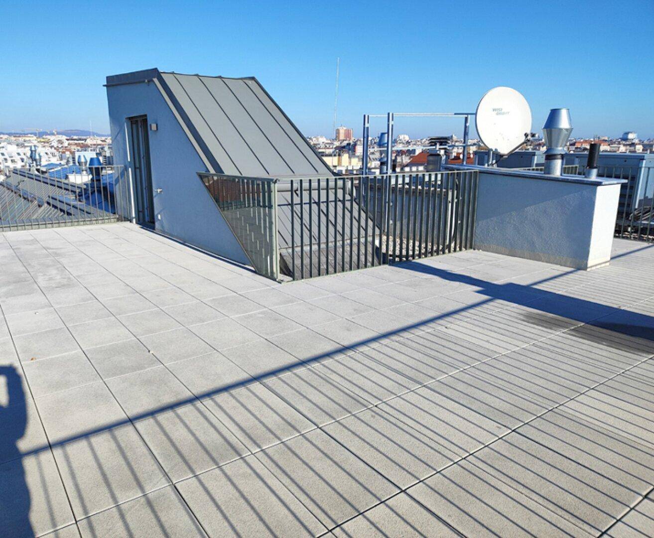Dachterrasse mit Fliesenboden, Metallgeländer und Zugang zu einem kleinen Dachaufbau.
