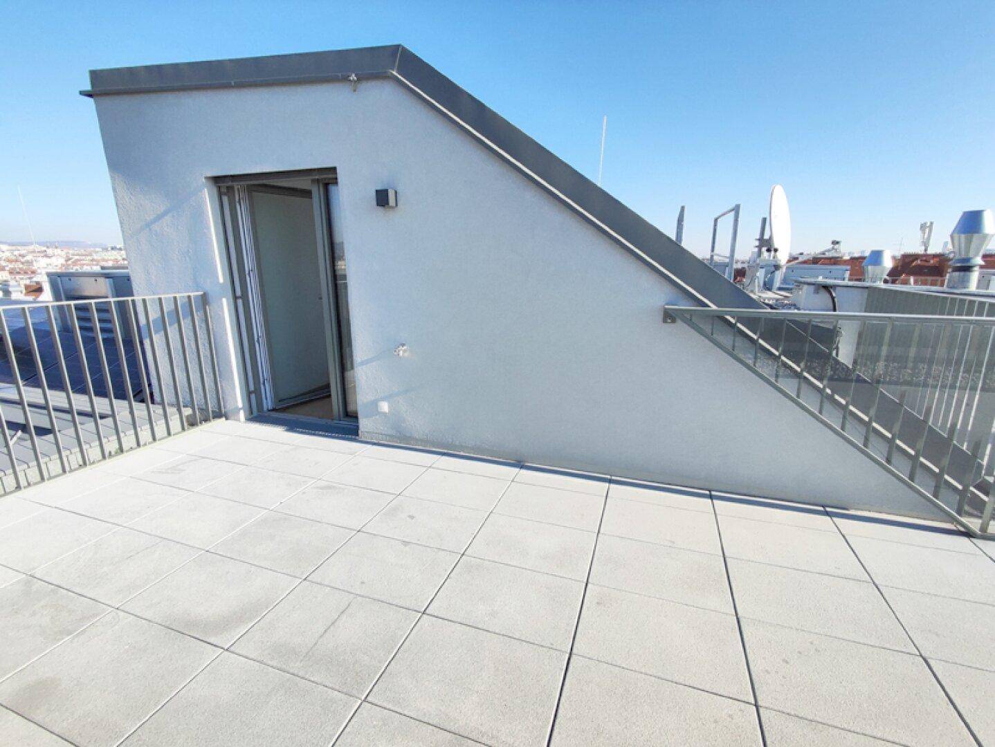 Dachterrasse mit Fliesenboden und Zugang zu einem Dachaufbau mit offener Tür.