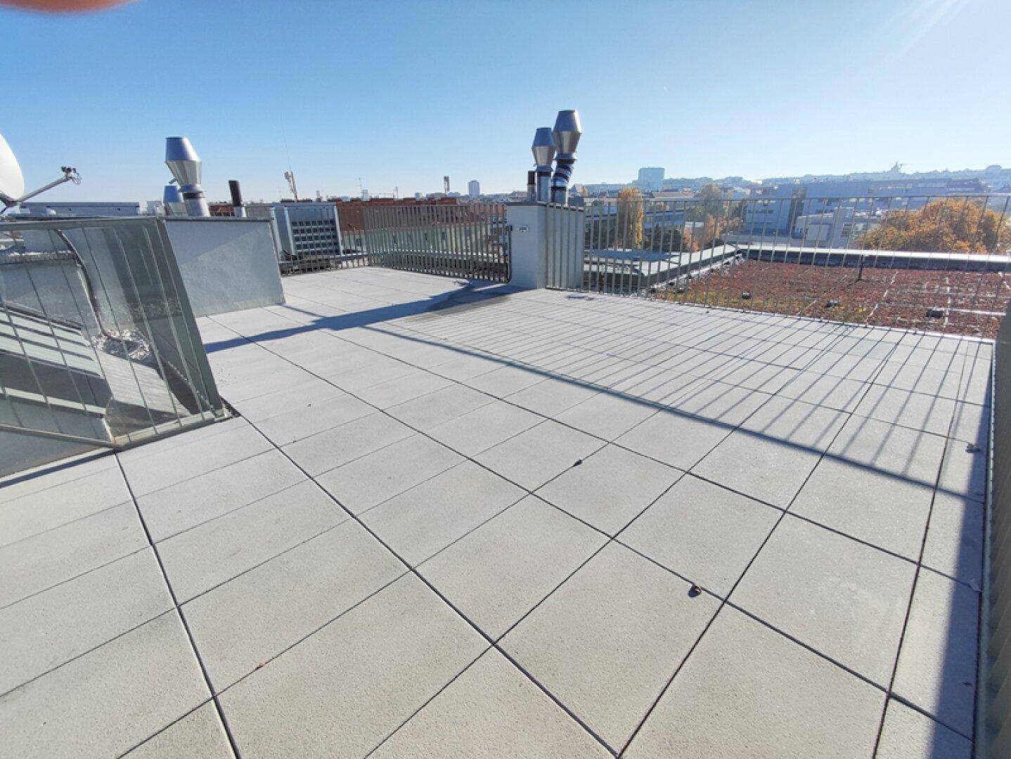 Dachterrasse mit Fliesenboden, Metallgeländer und Blick auf die Stadt und Gründächer.