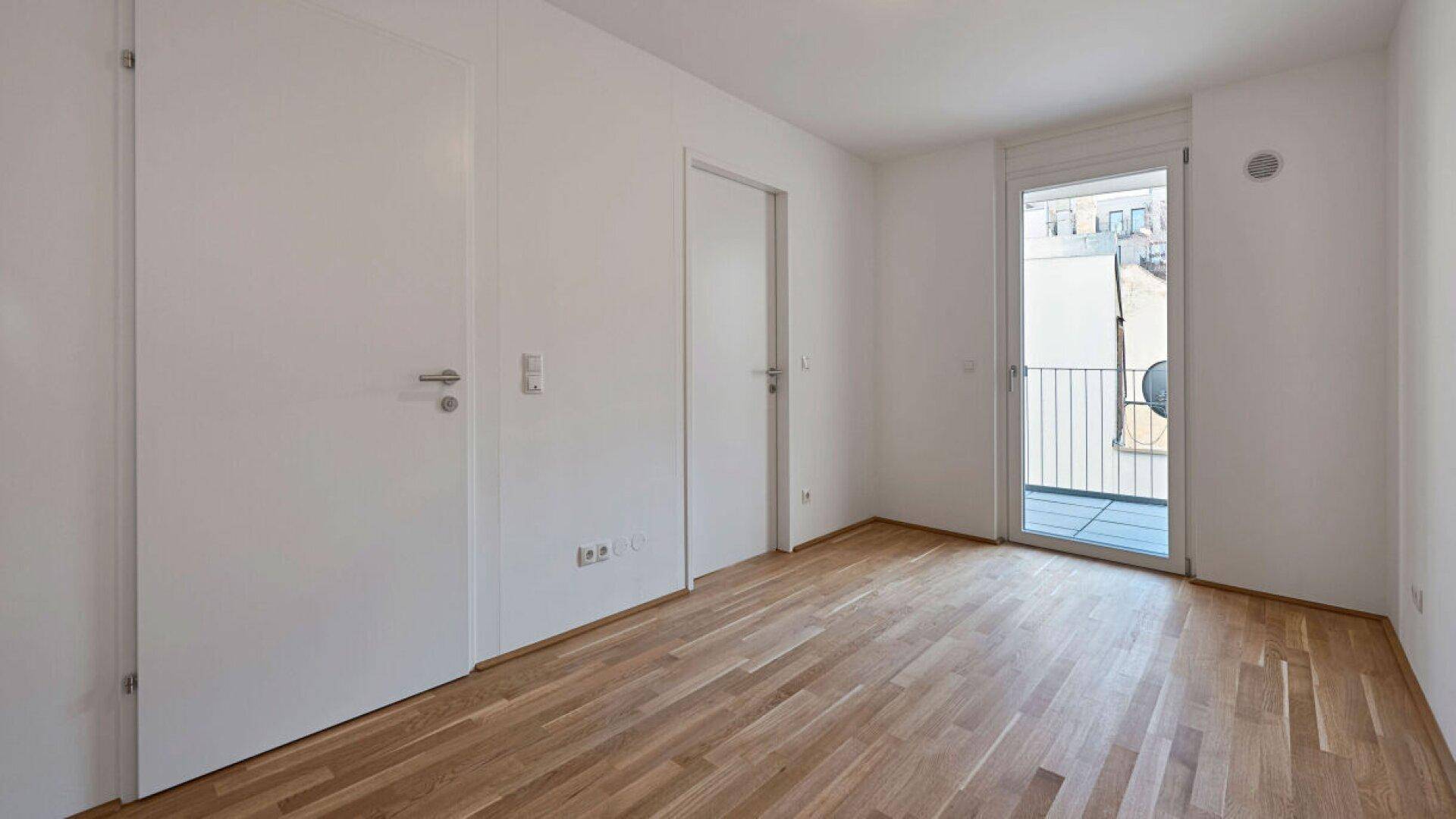 Geräumiges Schlafzimmer mit hellem Parkettboden und Balkontür.