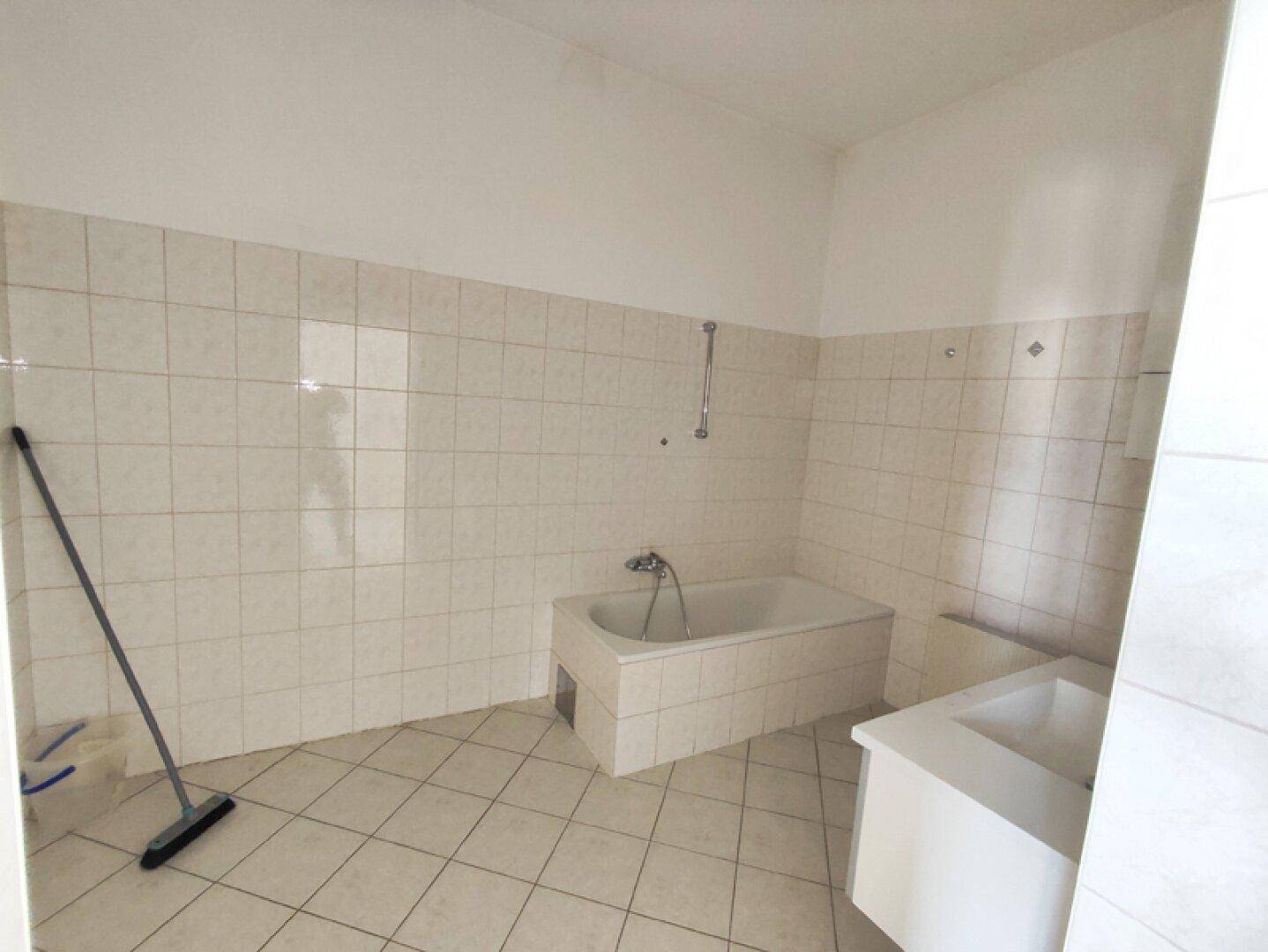 Badezimmer mit hellen Fliesen an Wänden und Boden, ausgestattet mit einer Badewanne.