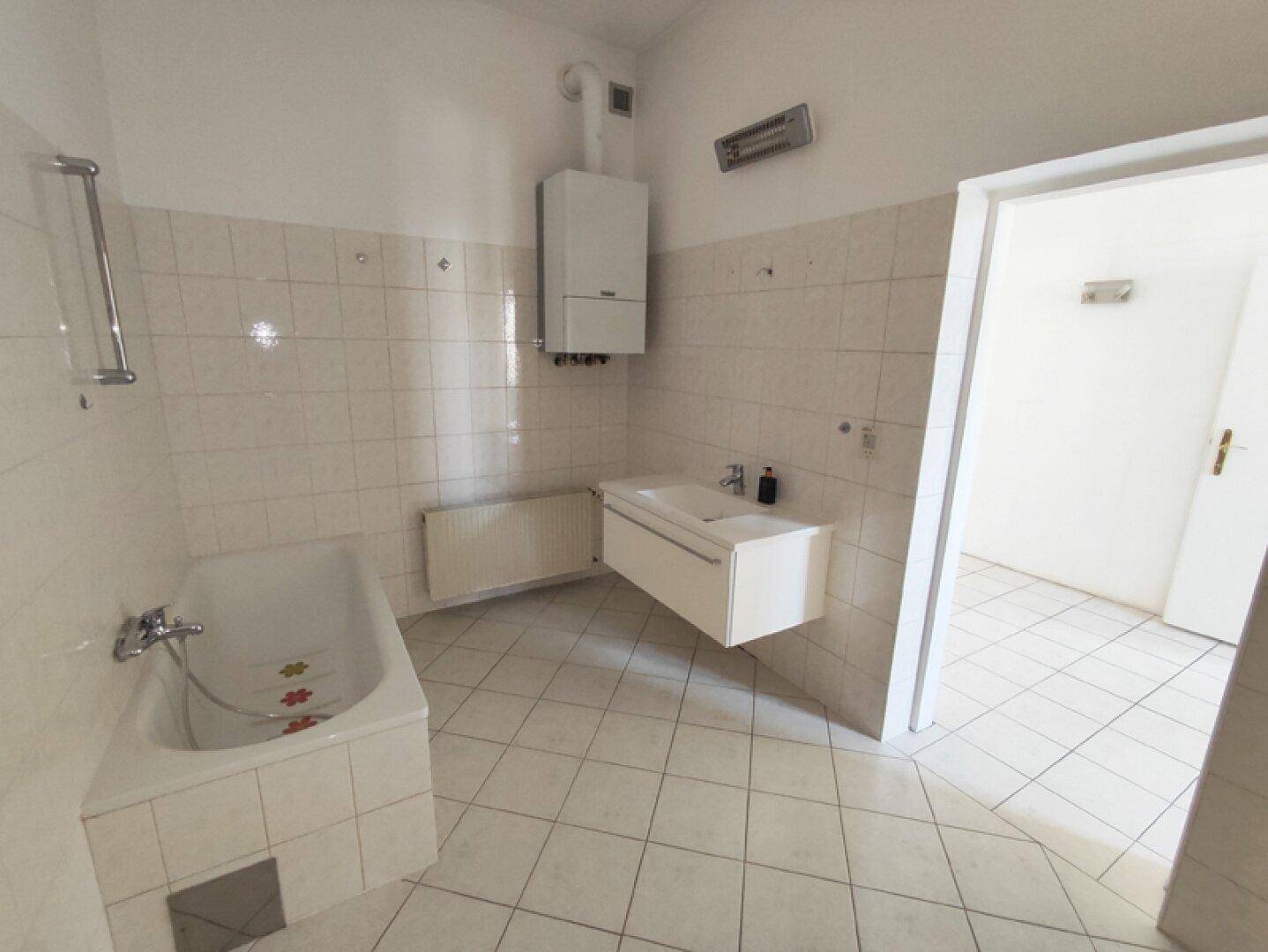 Helles Badezimmer mit Badewanne, Waschbecken und einem Heizkörper unter dem Warmwasserbereiter.