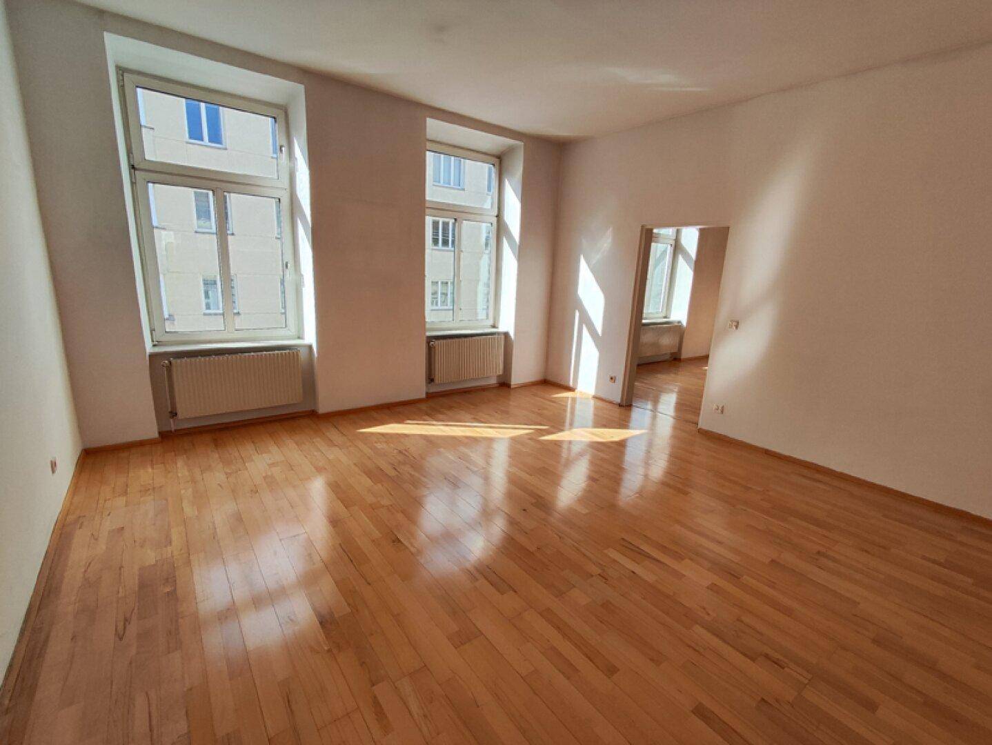 Geräumiges Zimmer mit hellem Parkettboden und Blick auf die umliegenden Gebäude.