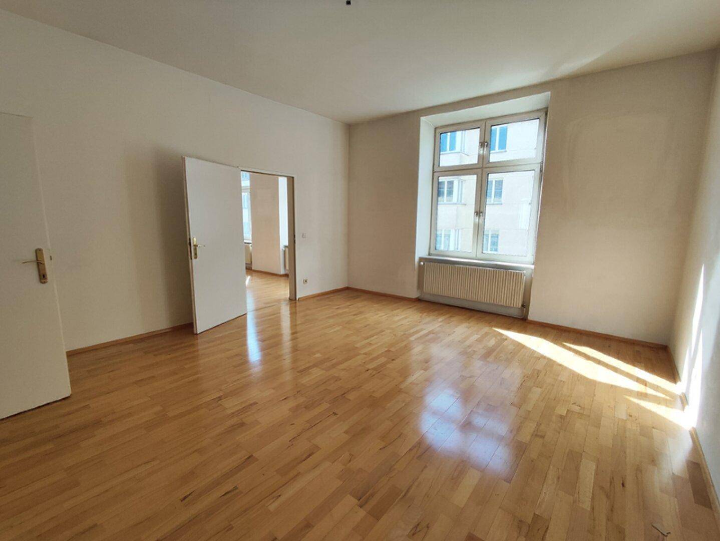 Geräumiges Zimmer mit Parkettboden und offener Tür zu einem weiteren Raum, ideal für flexible Nutzung.