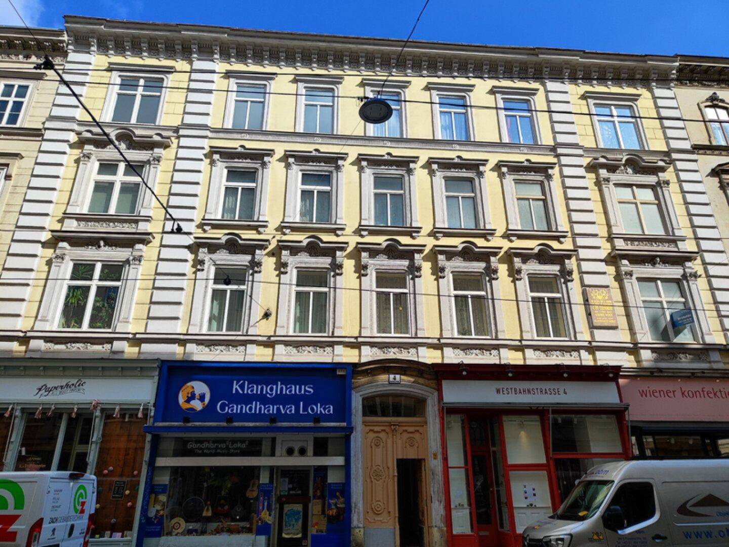 Historische Fassade eines Mehrfamilienhauses mit Geschäften im Erdgeschoss und vielen Fenstern.