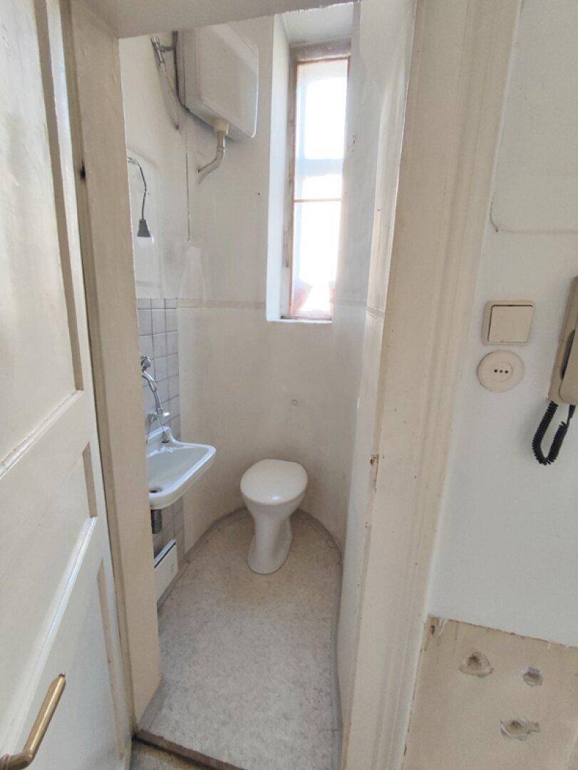 Kleines Gäste-WC mit Toilette, Waschbecken und schmalem Fenster, funktional und kompakt.