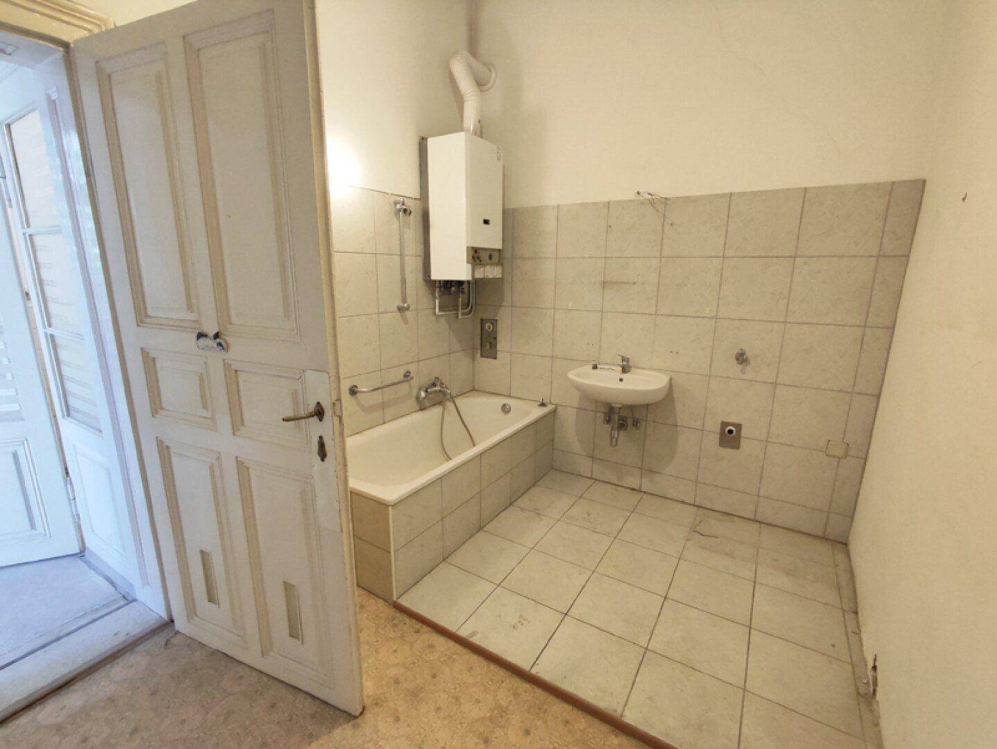 Badezimmer mit Badewanne, Waschbecken und Gastherme, bereit für eine Modernisierung.