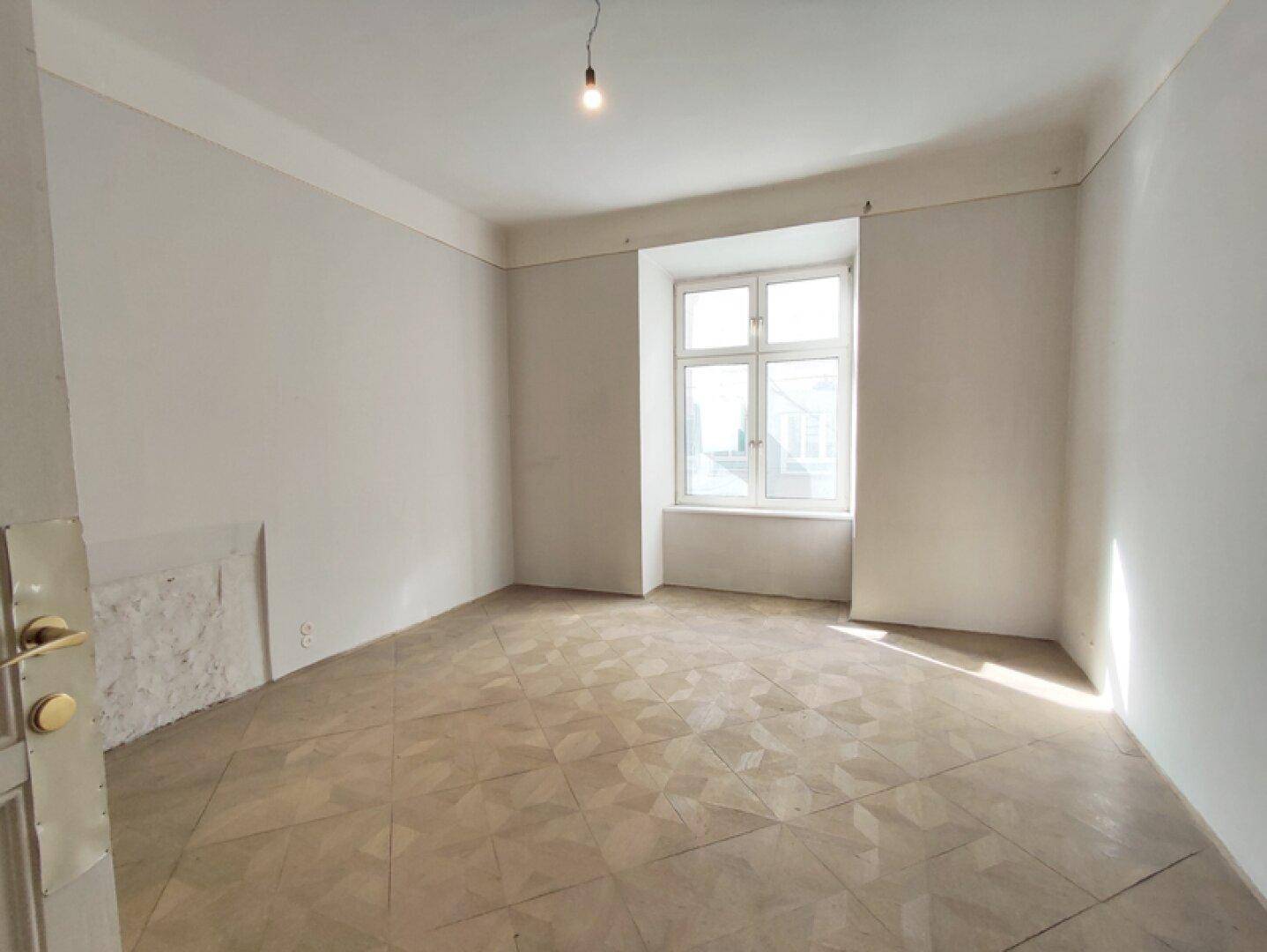 Geräumiges Zimmer mit klassischem Parkettboden und einem großen Fenster, ideal für individuelle Gestaltung.