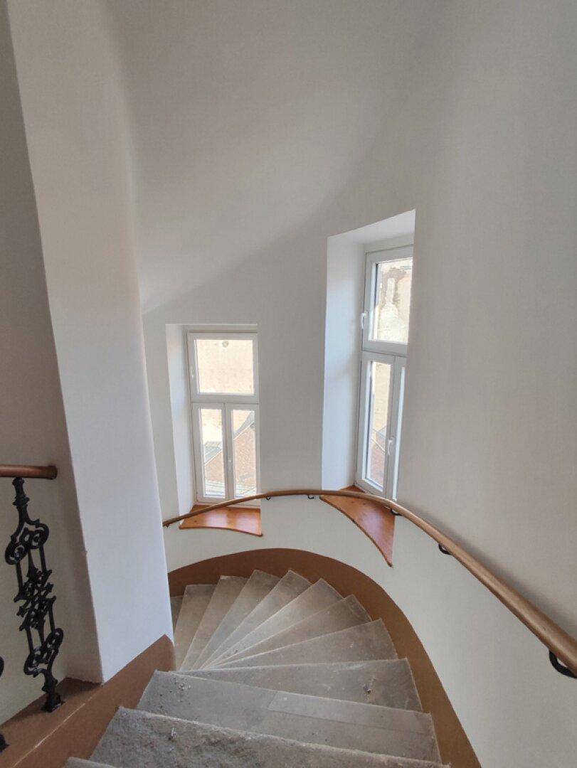 Elegantes Wendeltreppenhaus mit Holzgeländer und Fenstern, das Licht in die oberen Etagen bringt.