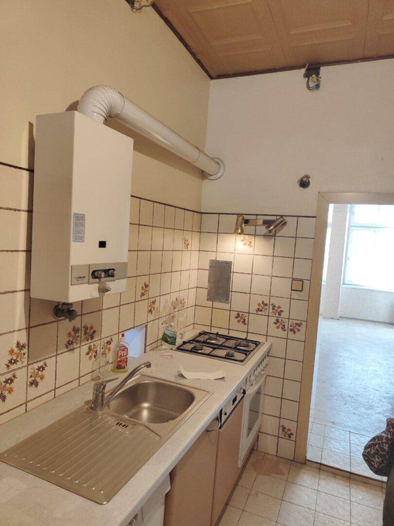 Detailansicht der Küche mit Gasherd, Spüle und Wandfliesen, renovierungsbedürftig.