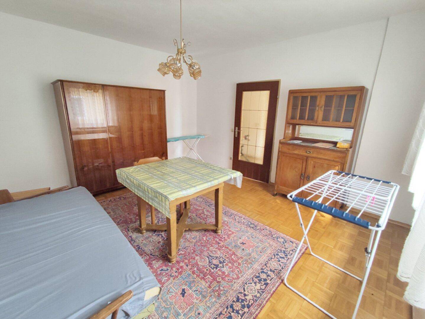 Schlichtes Zimmer mit Holzboden, Kleiderschrank und Wäscheständer.