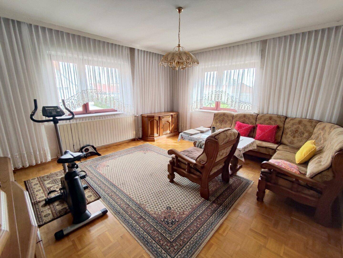 Gemütliches Wohnzimmer mit traditionellen Möbeln, Parkettboden und großen Fenstern.