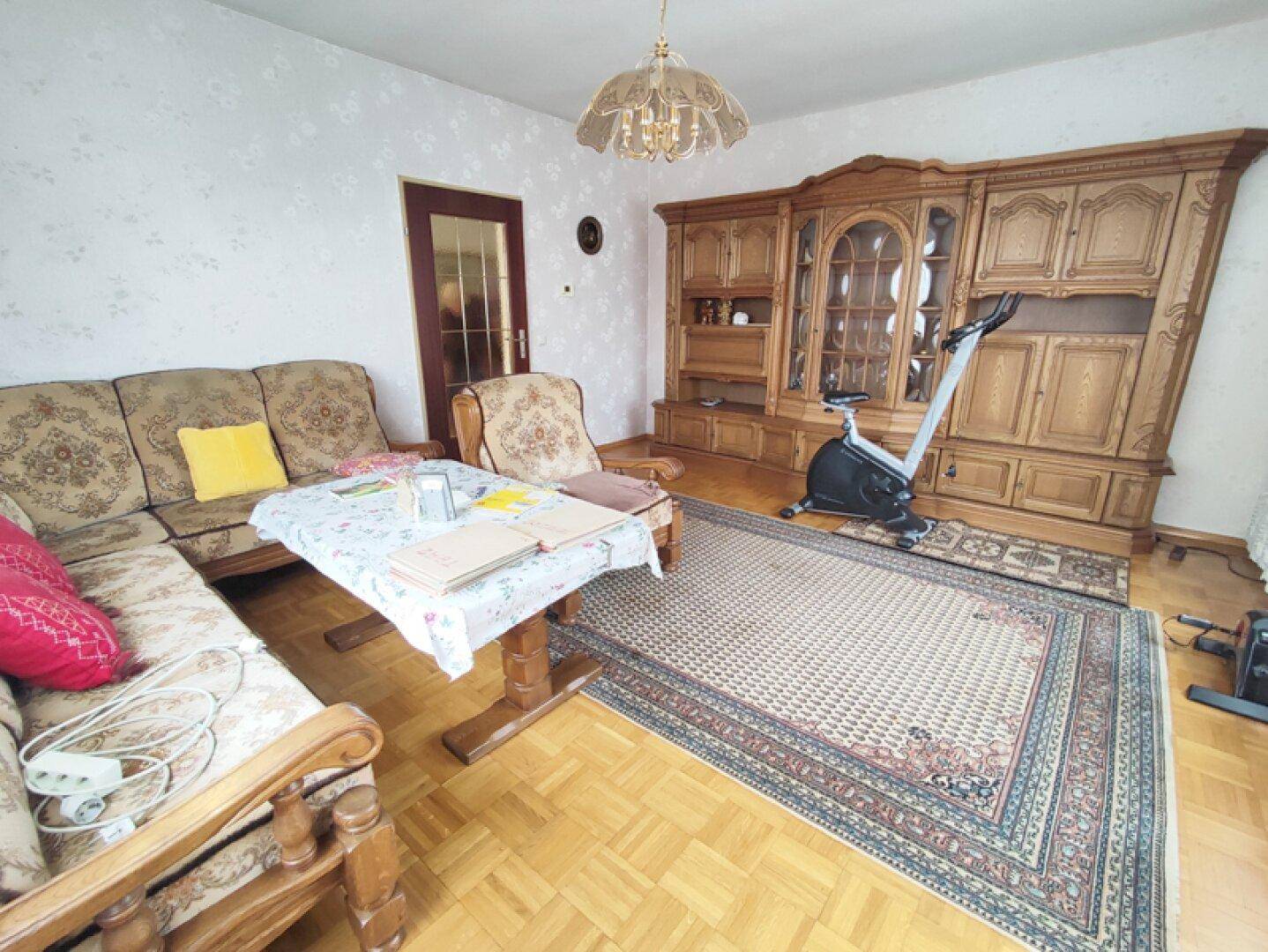 Wohnzimmer mit klassischer Holzschrankwand, Parkettboden und Heimtrainer.