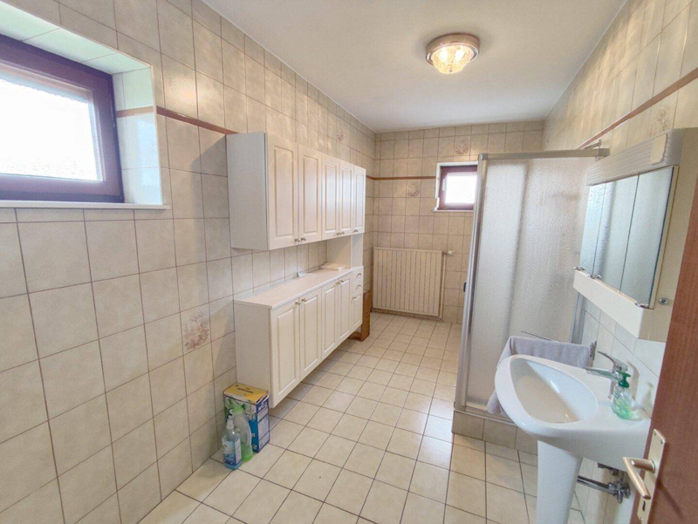 Geräumiges Badezimmer mit hellen Fliesen, Duschkabine und Waschbecken.