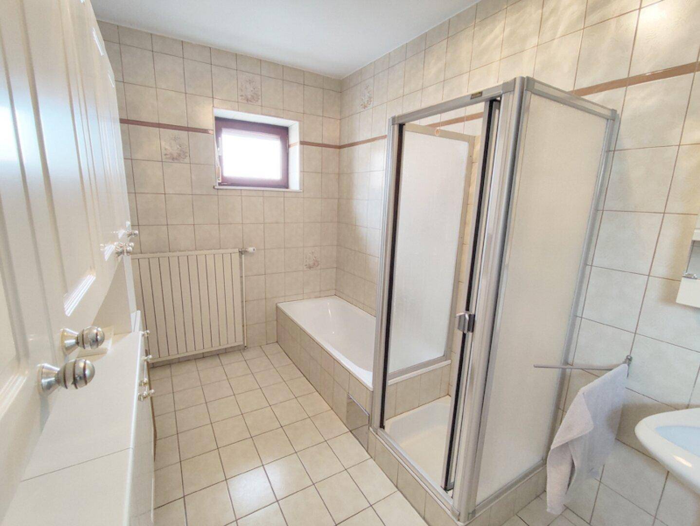 Helles Badezimmer mit Badewanne, Duschkabine und Heizkörper.