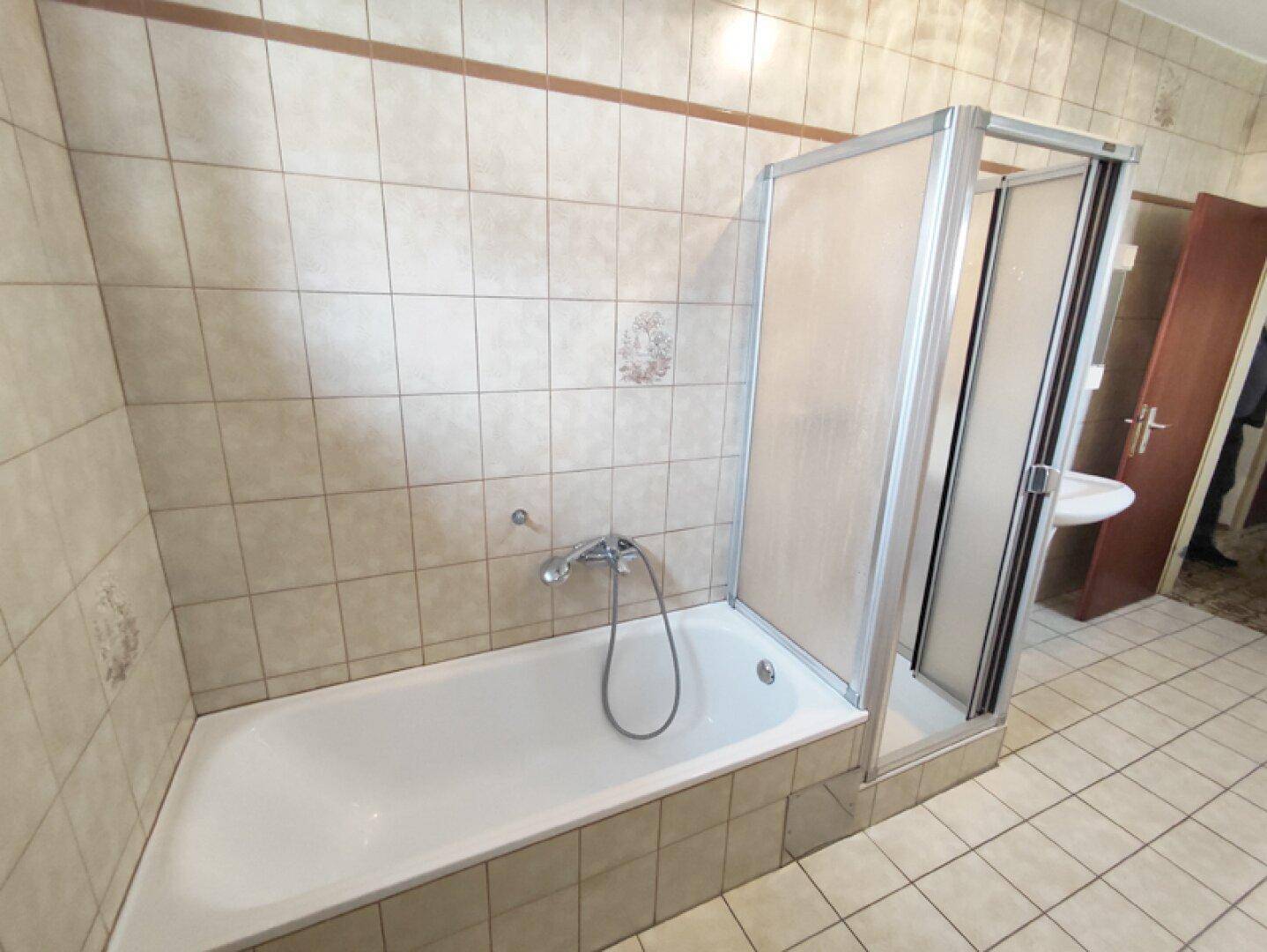 Badezimmer mit Badewanne, Duschkabine und Zugang zu einem weiteren Raum.