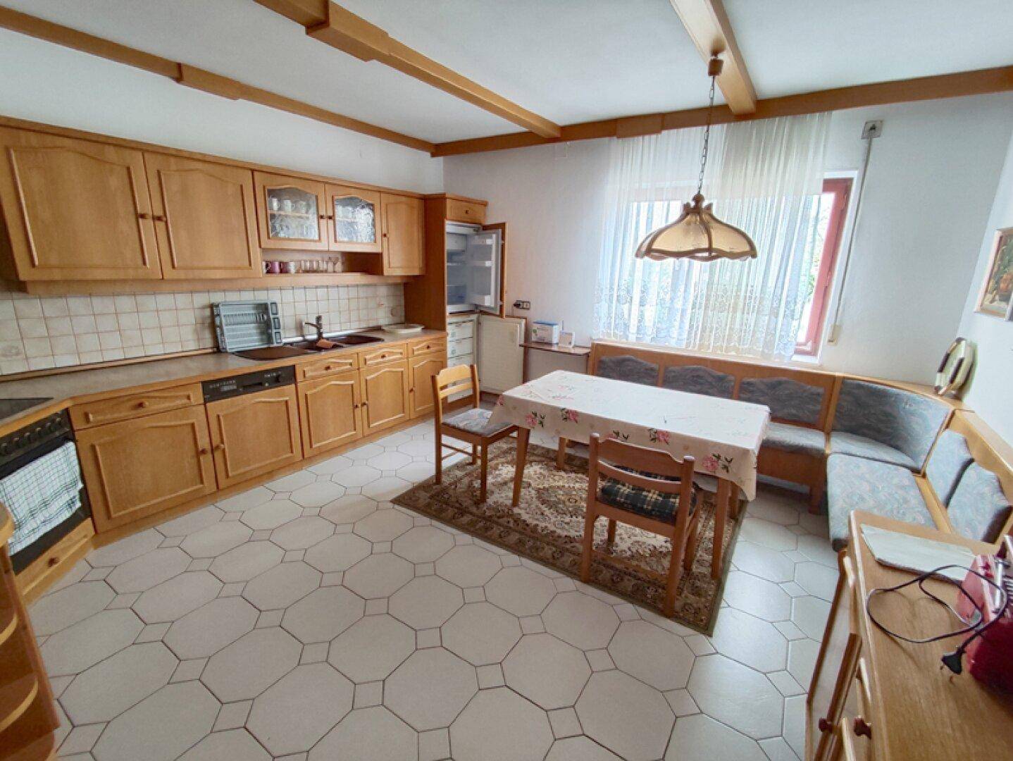 Voll ausgestattete Küche mit Holzschränken, Essbereich und Fenster mit Vorhängen.