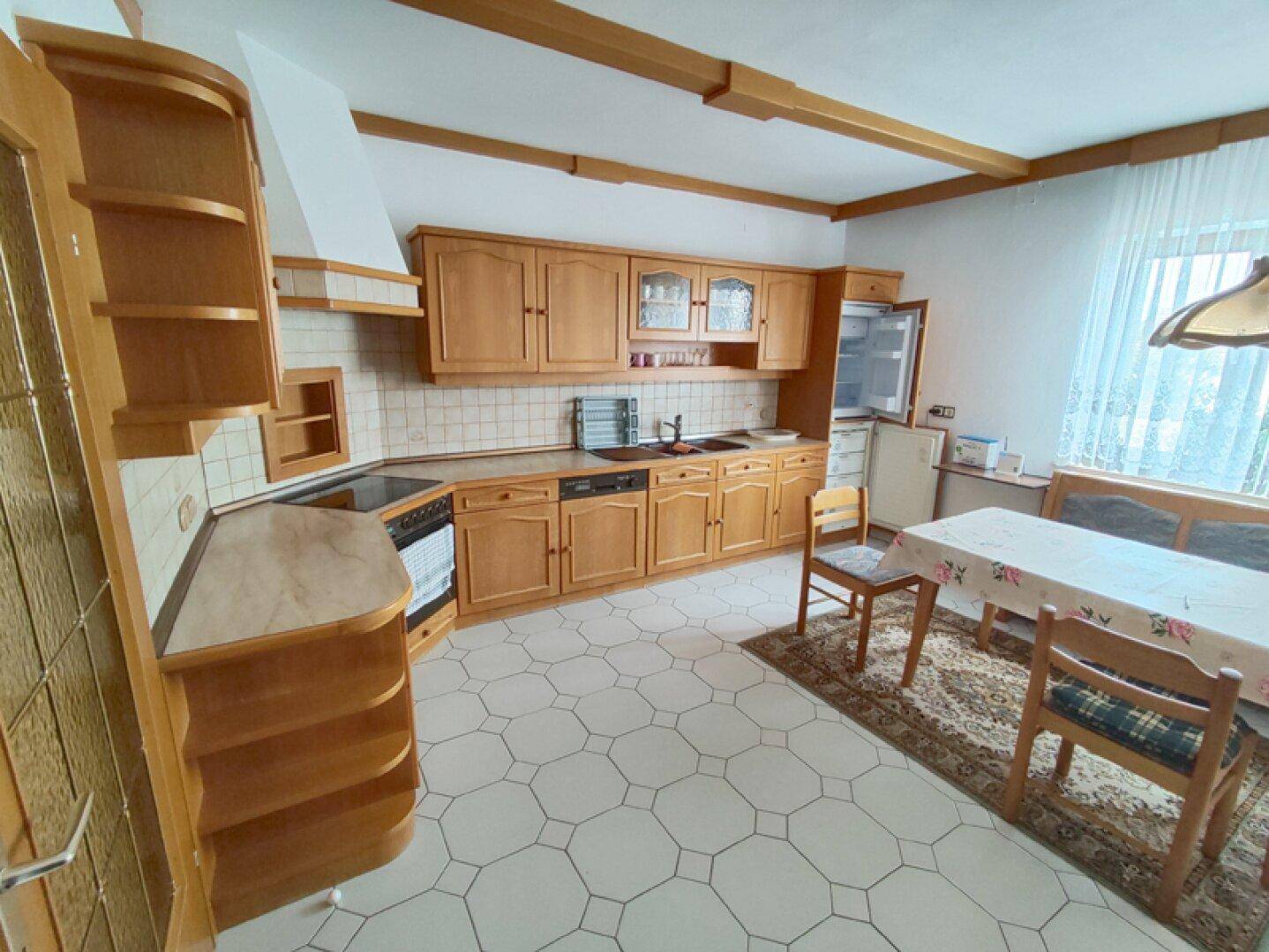 Helle Küche mit Holzschränken, Essbereich und Blick nach draußen.