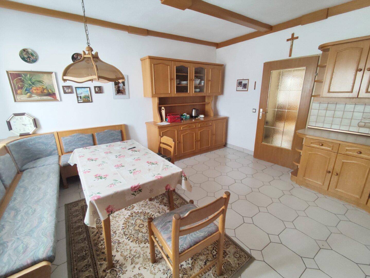 Geräumige Wohnküche mit Holzbalken, Essecke und traditionellen Küchenschränken.