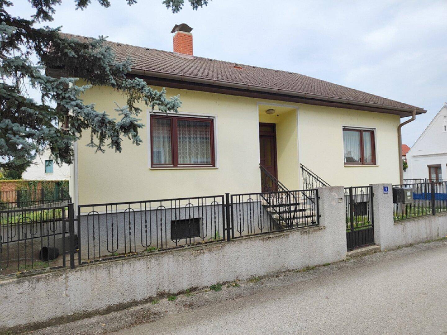 Einfamilienhaus mit gelber Fassade und braunem Dach in ländlicher Umgebung.