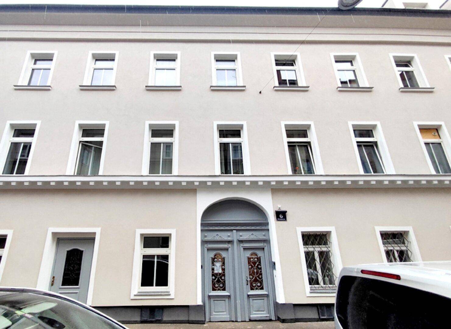 Klassische Fassade eines Mehrfamilienhauses mit vielen Fenstern und einer eleganten Eingangstür.