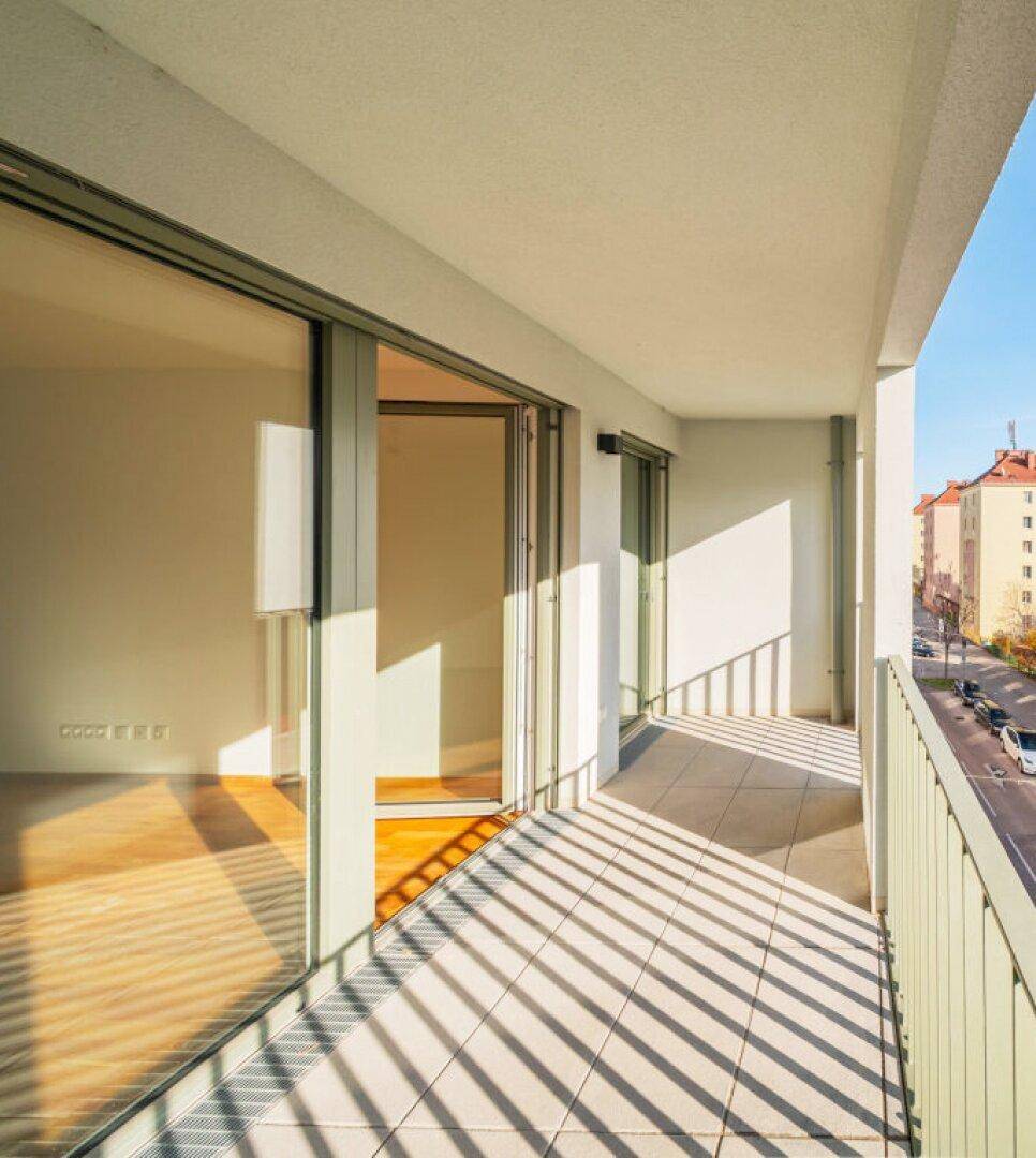 Sonniger Balkon mit Fliesenboden und Blick auf die Straße und umliegende Gebäude.