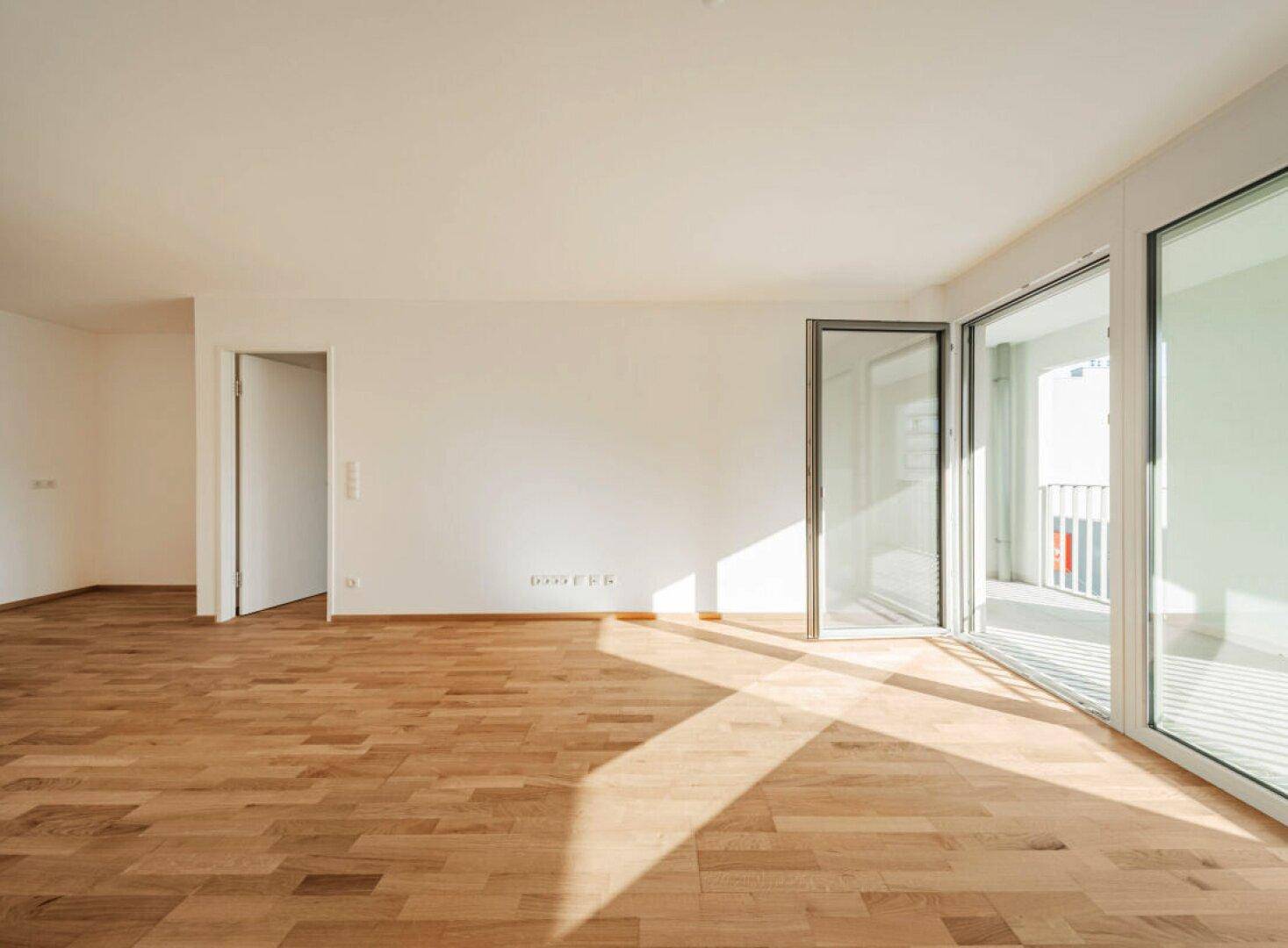 Geräumiges, helles Wohnzimmer mit Holzboden und großen Fenstern, die viel Tageslicht hereinlassen.