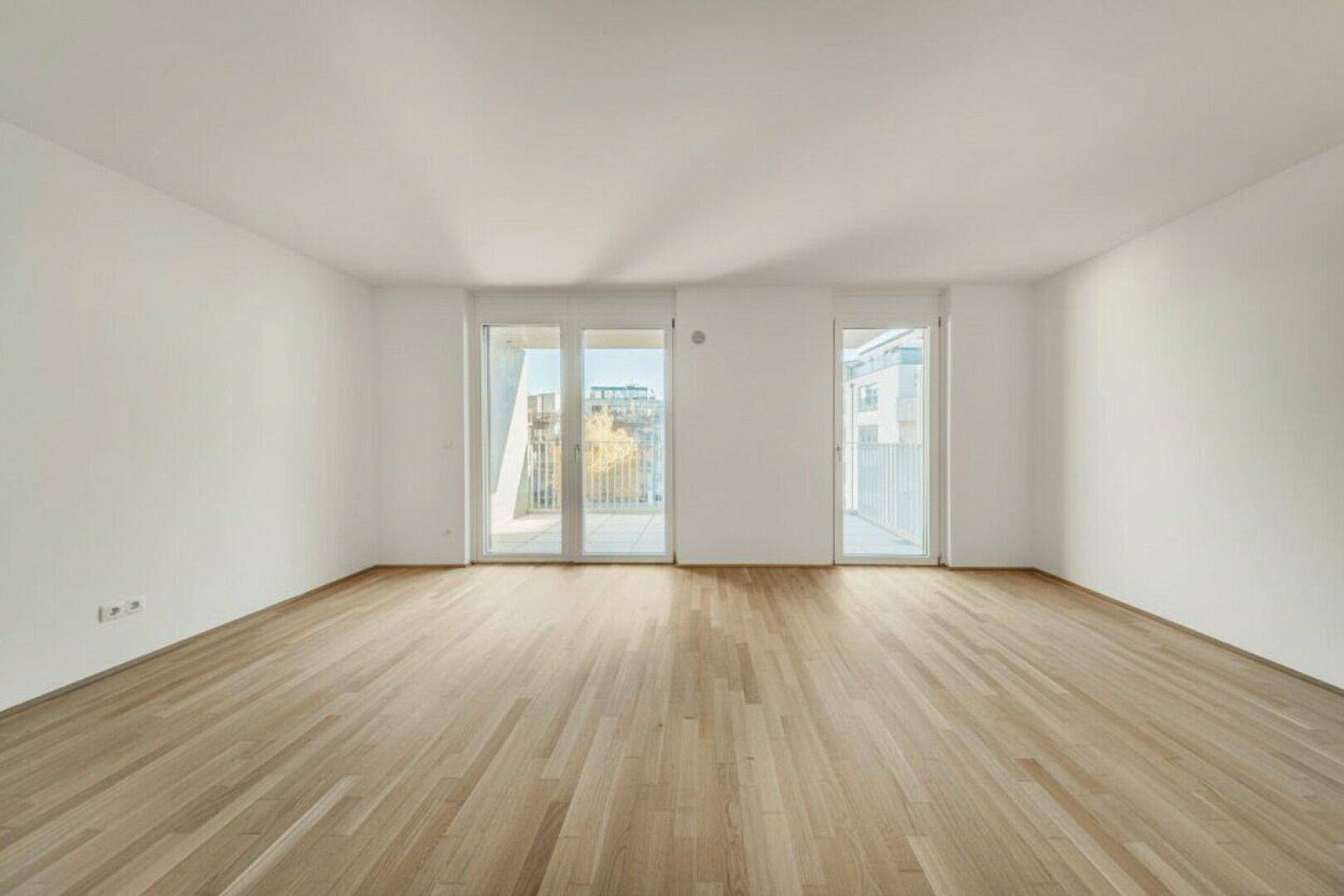 Geräumiges Wohnzimmer mit hellem Parkettboden und zwei Balkontüren, bietet viel natürliches Licht.