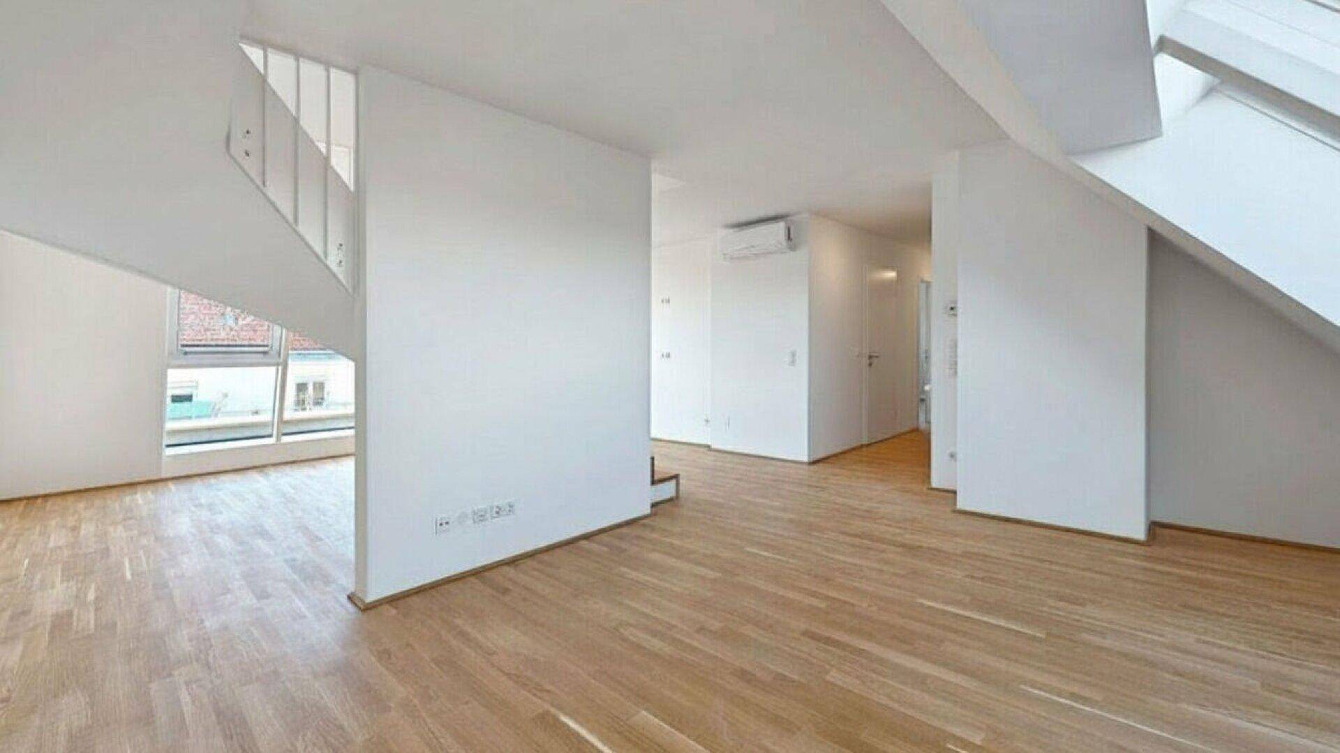 Geräumiger, heller Wohnbereich mit Holzparkettboden und schrägen Wänden im Dachgeschoss.