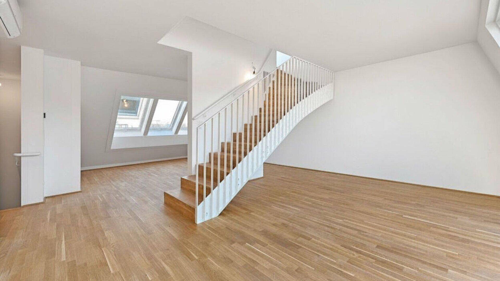 Geräumiger Wohnbereich mit Holzparkettboden und eleganter Treppe, die in das obere Geschoss führt.