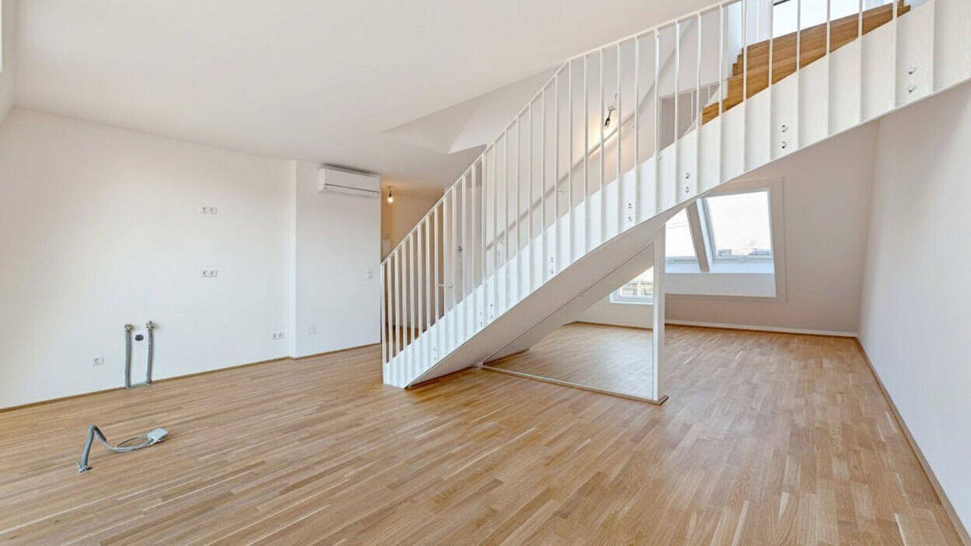 Heller Wohnbereich mit Holzparkettboden, moderner Treppe und großen Dachfenstern.