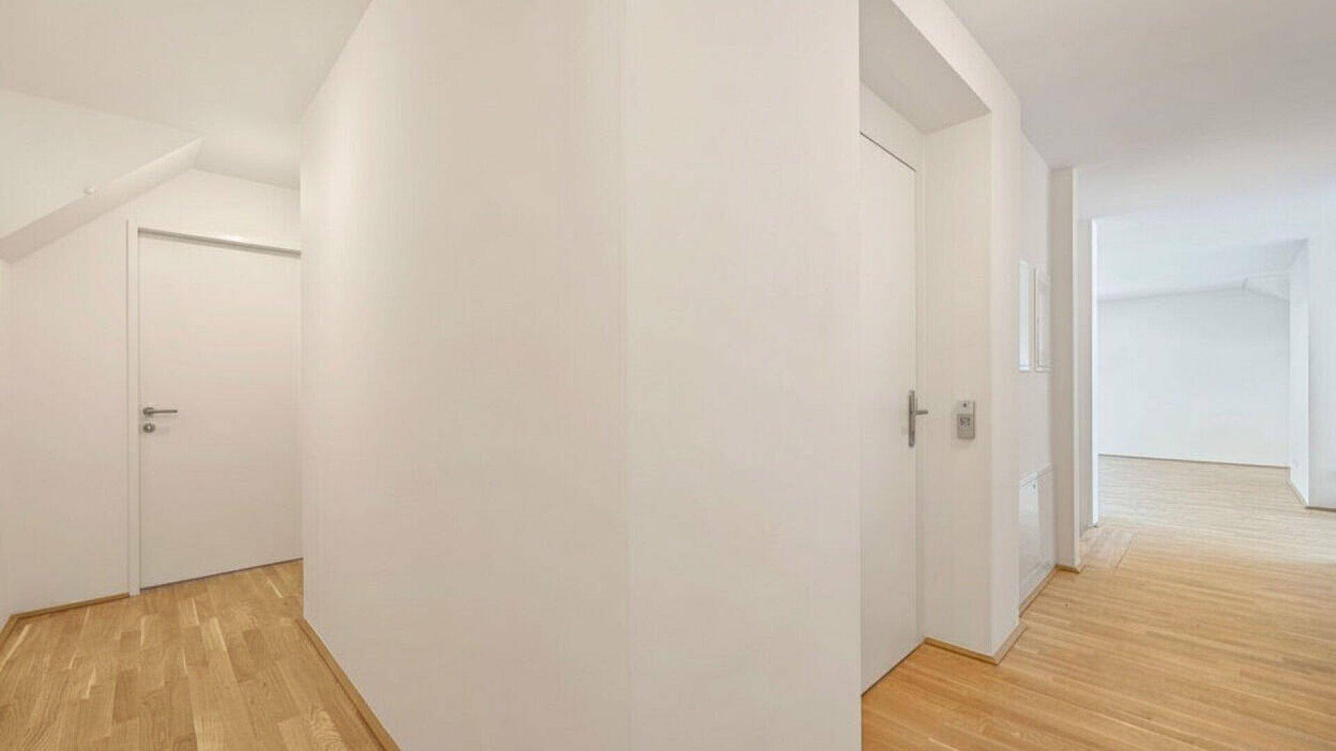 Heller Flur mit Holzparkettboden und weißen Wänden, der zu verschiedenen Räumen führt.