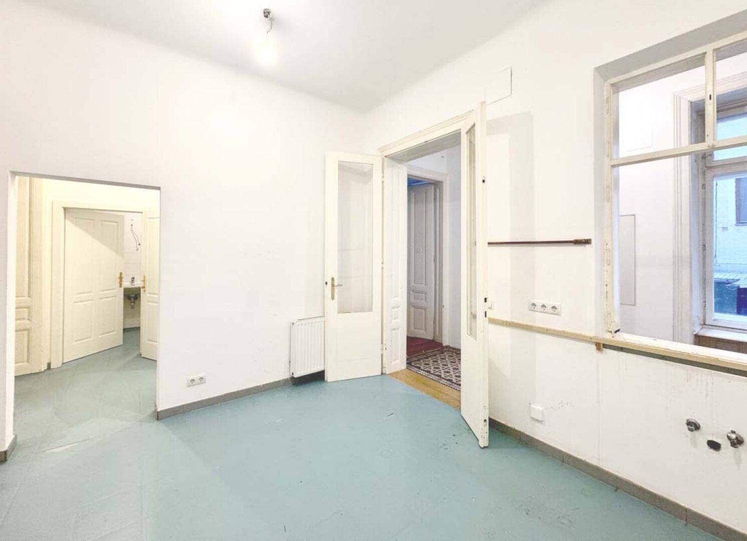 Leerer Raum mit hellblauem Boden, mehreren Türen und einem Fenster.