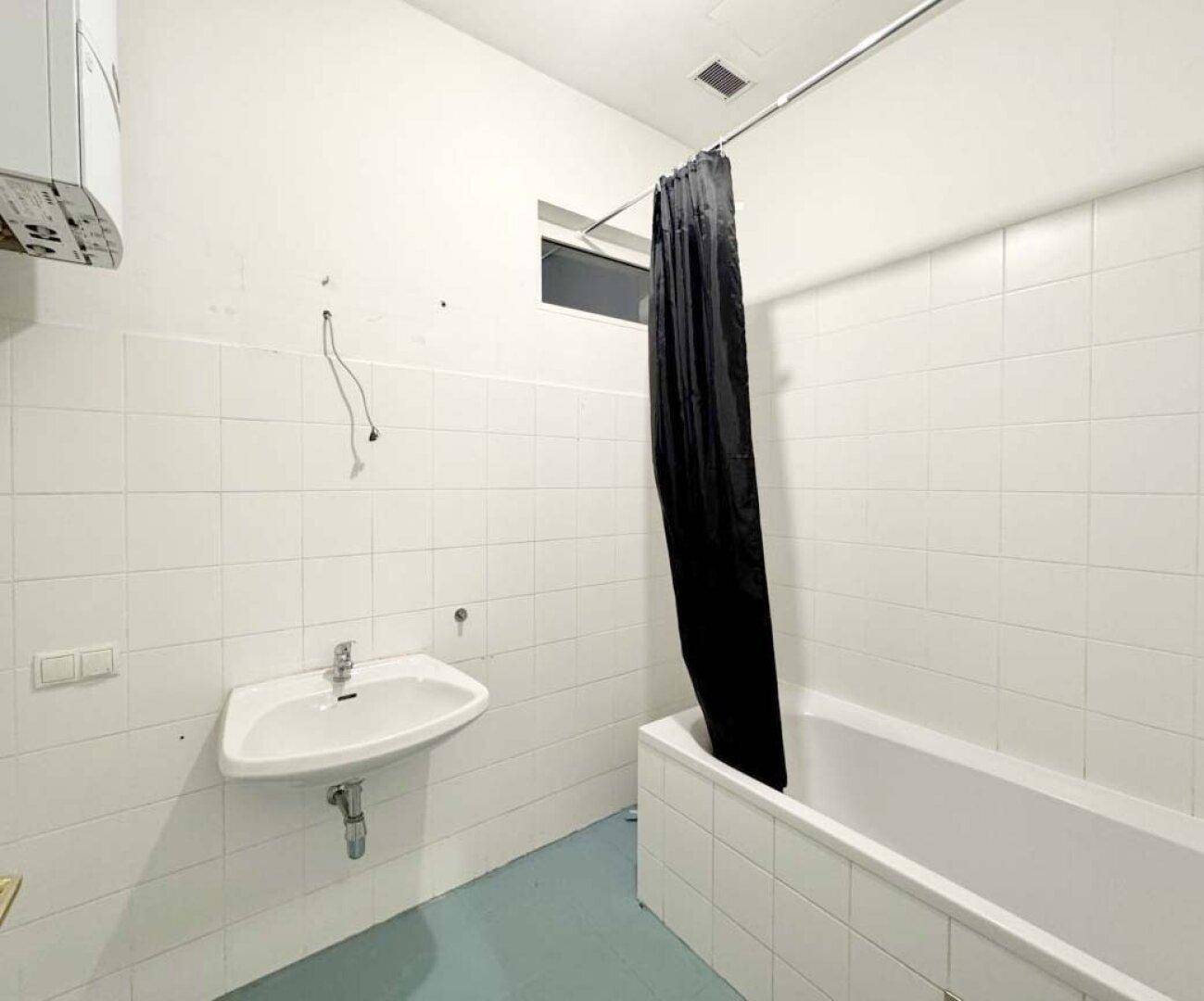 Badezimmer mit weiß gefliesten Wänden, Badewanne, Waschbecken und kleinem Fenster.