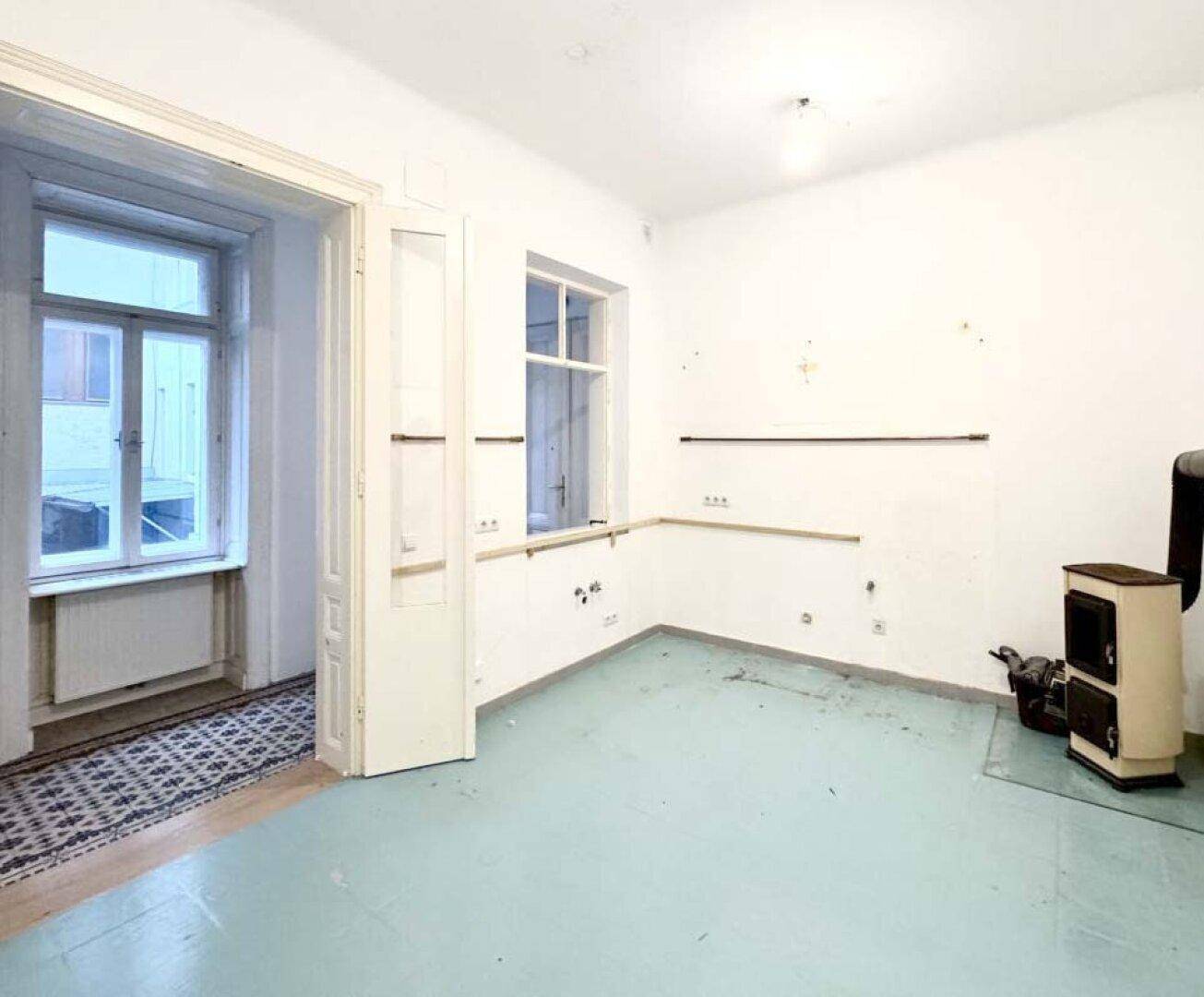 Leerer Raum mit hellblauem Boden, Fenster und einem traditionellen Holzofen.