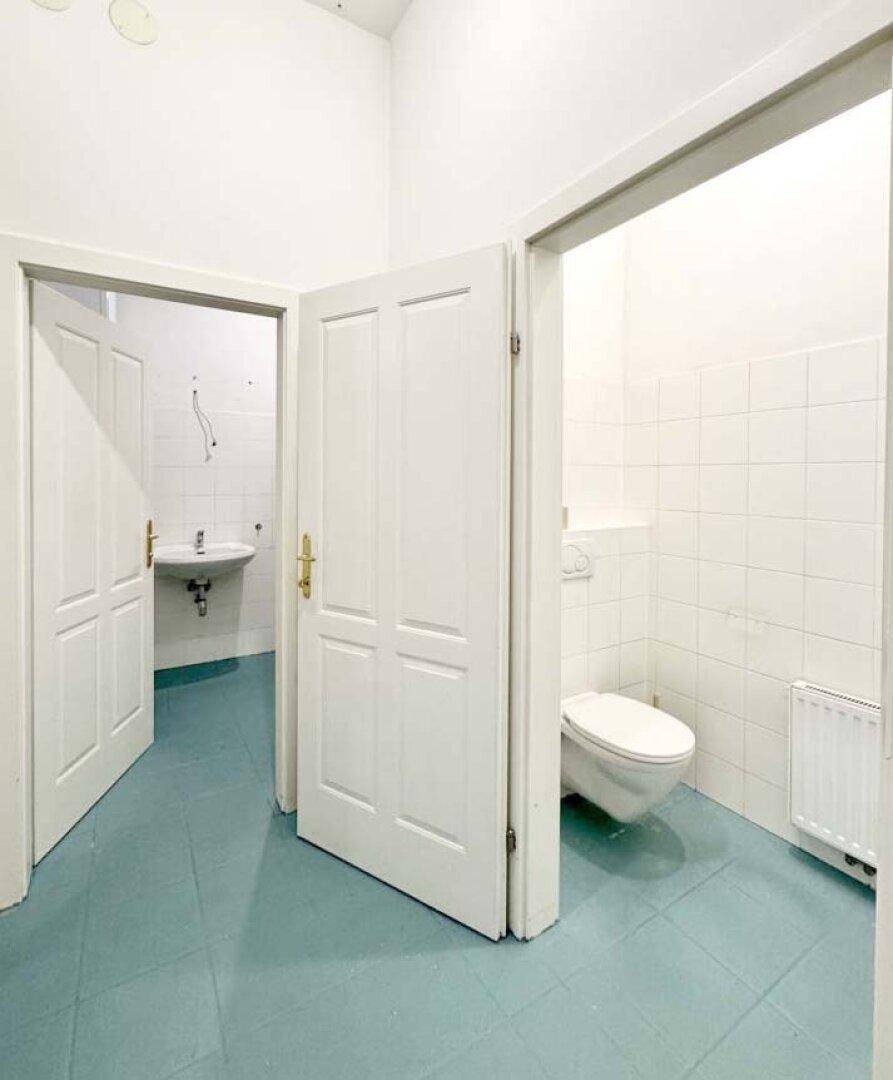 Separates WC mit wandmontierter Toilette, Waschbecken und weiß gefliesten Wänden.