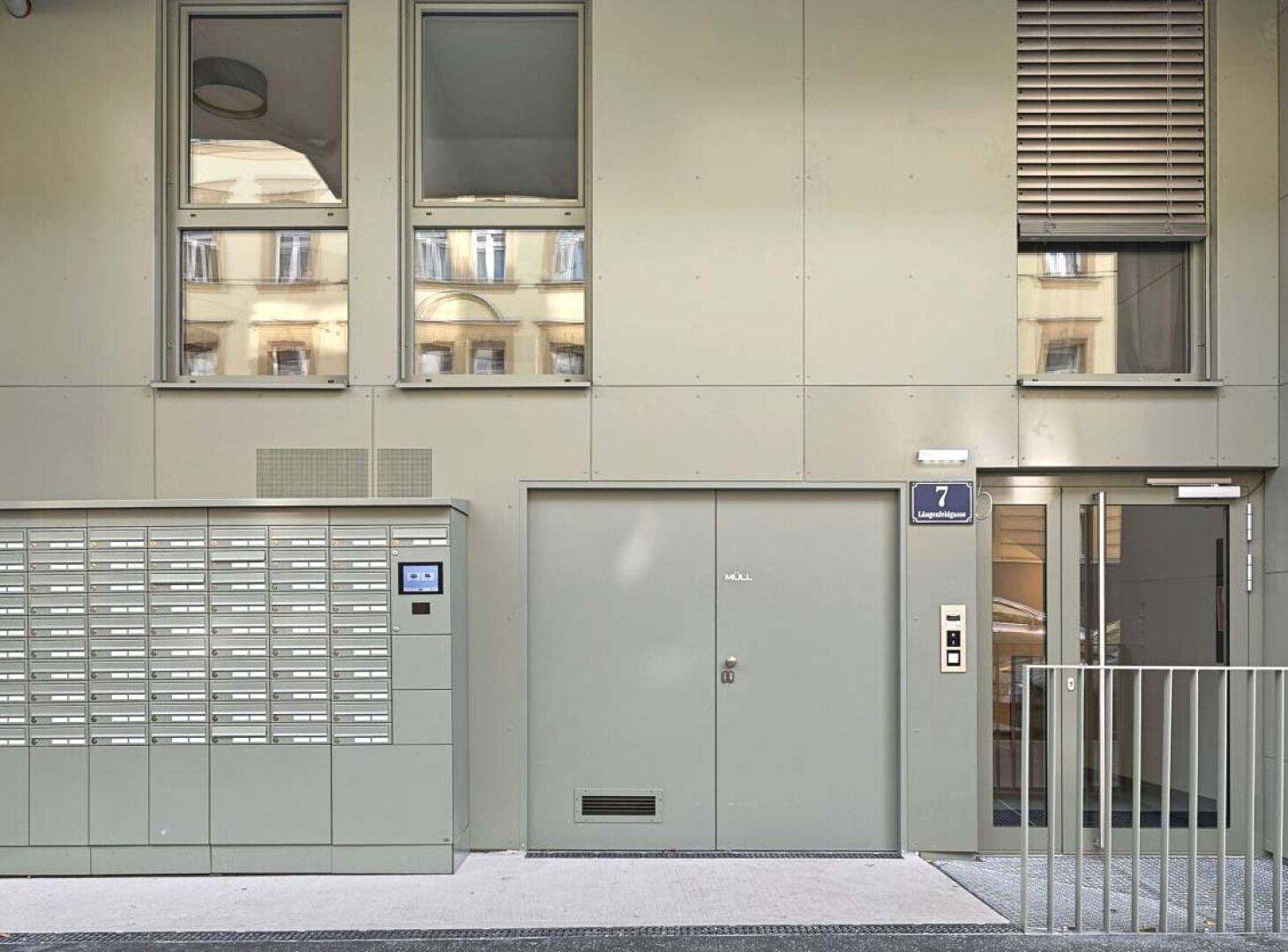 Moderner Hauseingang mit Briefkästen und großen Fenstern, integriert in eine schlichte Fassade.