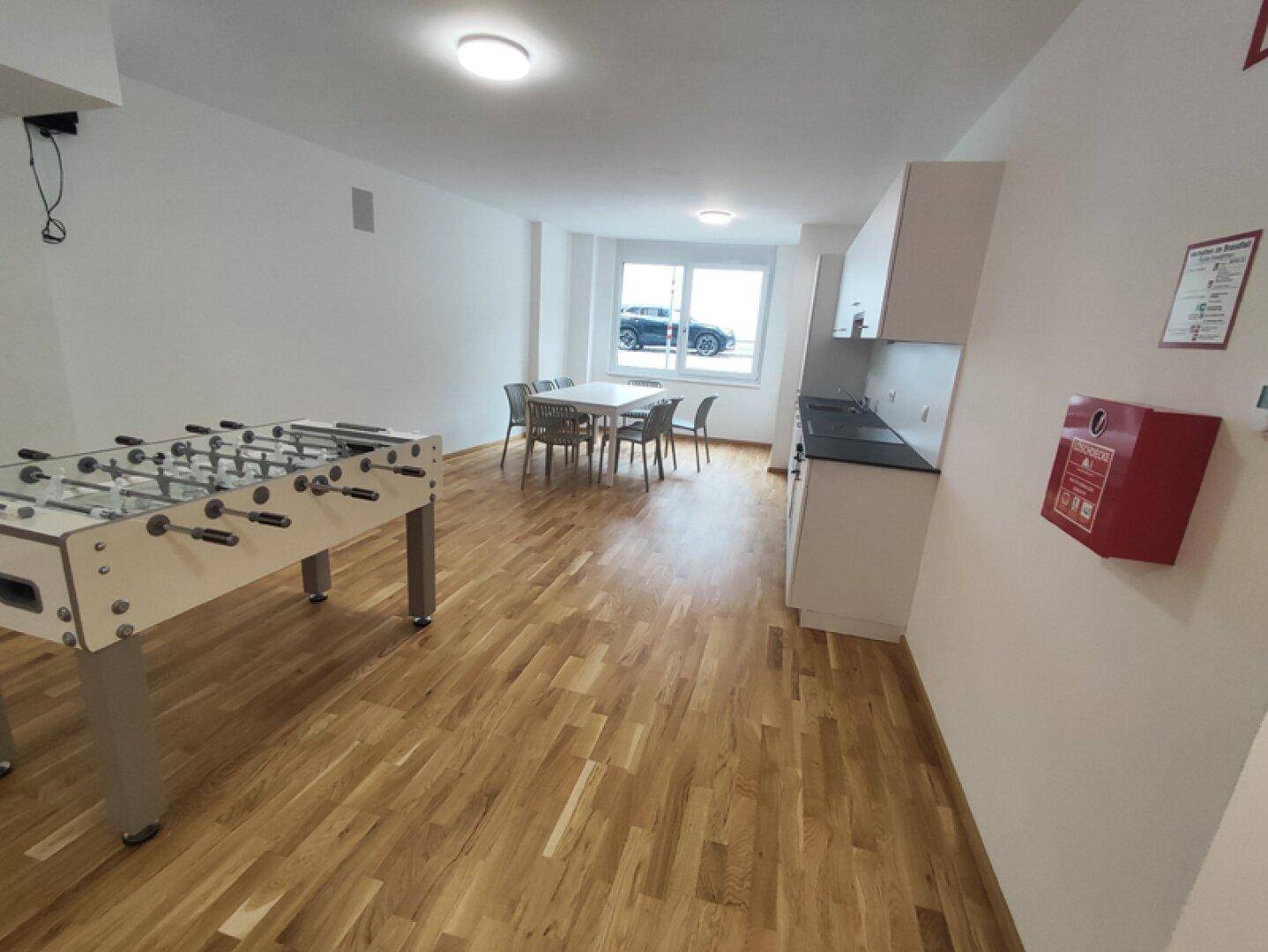 Geräumiger Spielraum mit Holzfußboden, Kickertisch, Esstisch und kleiner Küchenzeile.