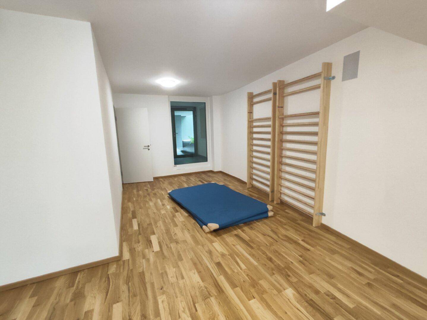 Heller Raum mit Holzfußboden, Sprossenwand und blauer Sportmatte, ideal für sportliche Aktivitäten.