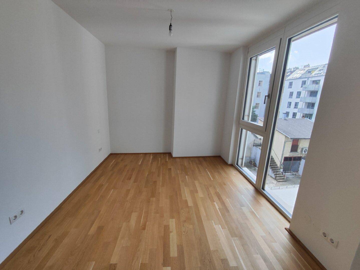 Helles Schlafzimmer mit großen Fenstern, Parkettboden und Blick auf die Umgebung.